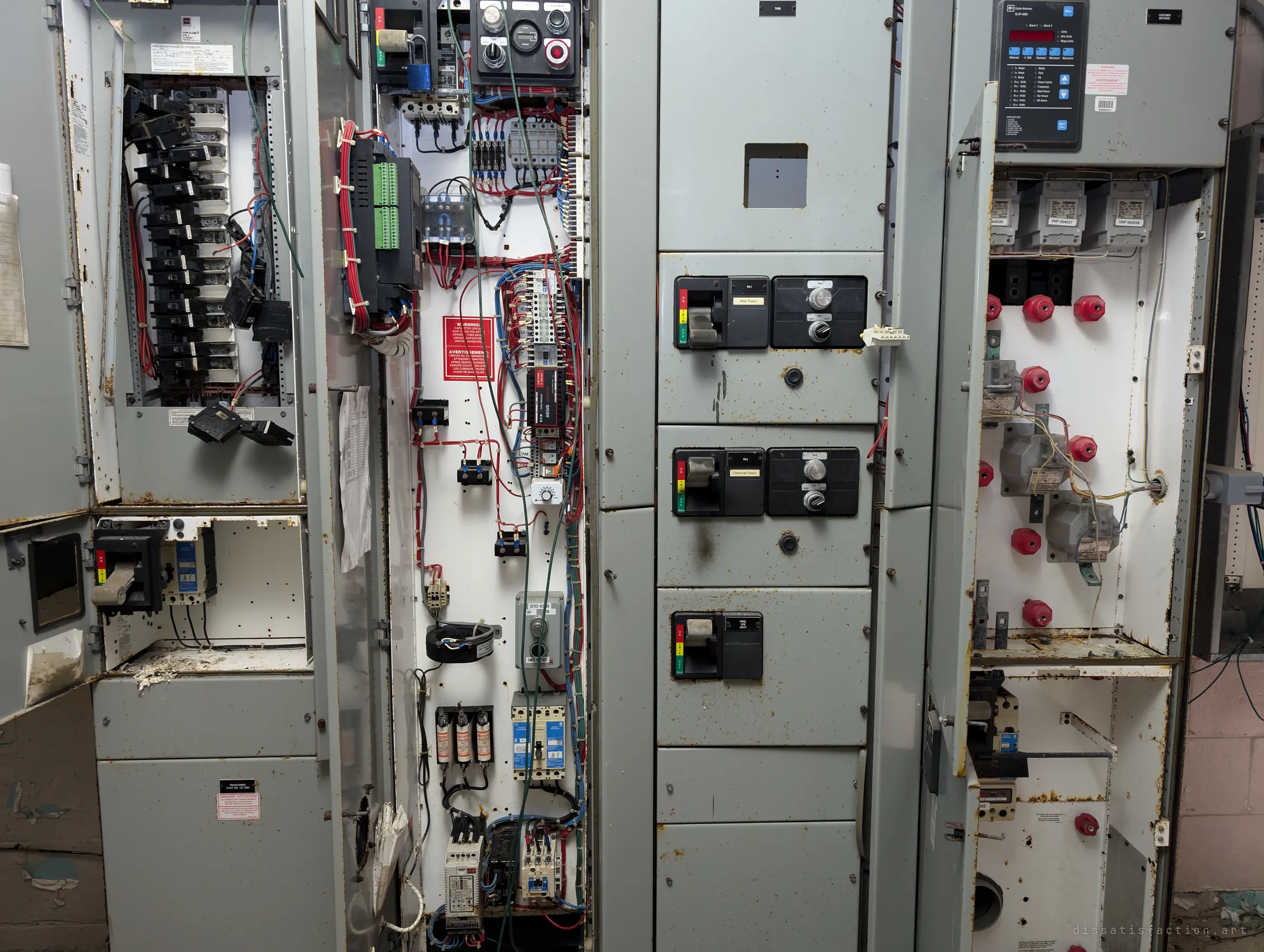 A close look at the opened motor control cabinets: loose breakers, tangled red and blue wiring and bilingual warning labels. It shows how thoroughly the electrics have been stripped and left exposed.