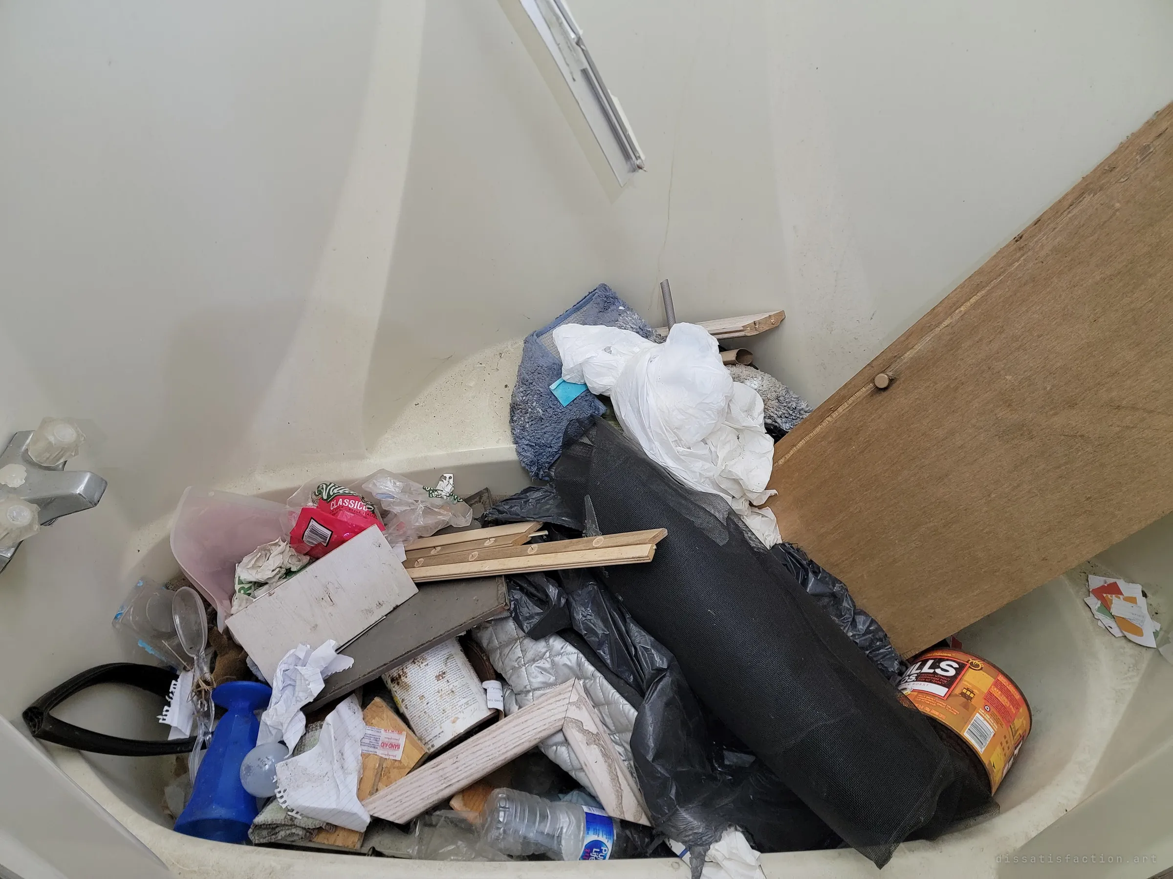 The bathtub is heaped with trash: bags, screen mesh, a coffee tin, crumpled notebook paper and a leaning board. The bathroom became the dumping ground.