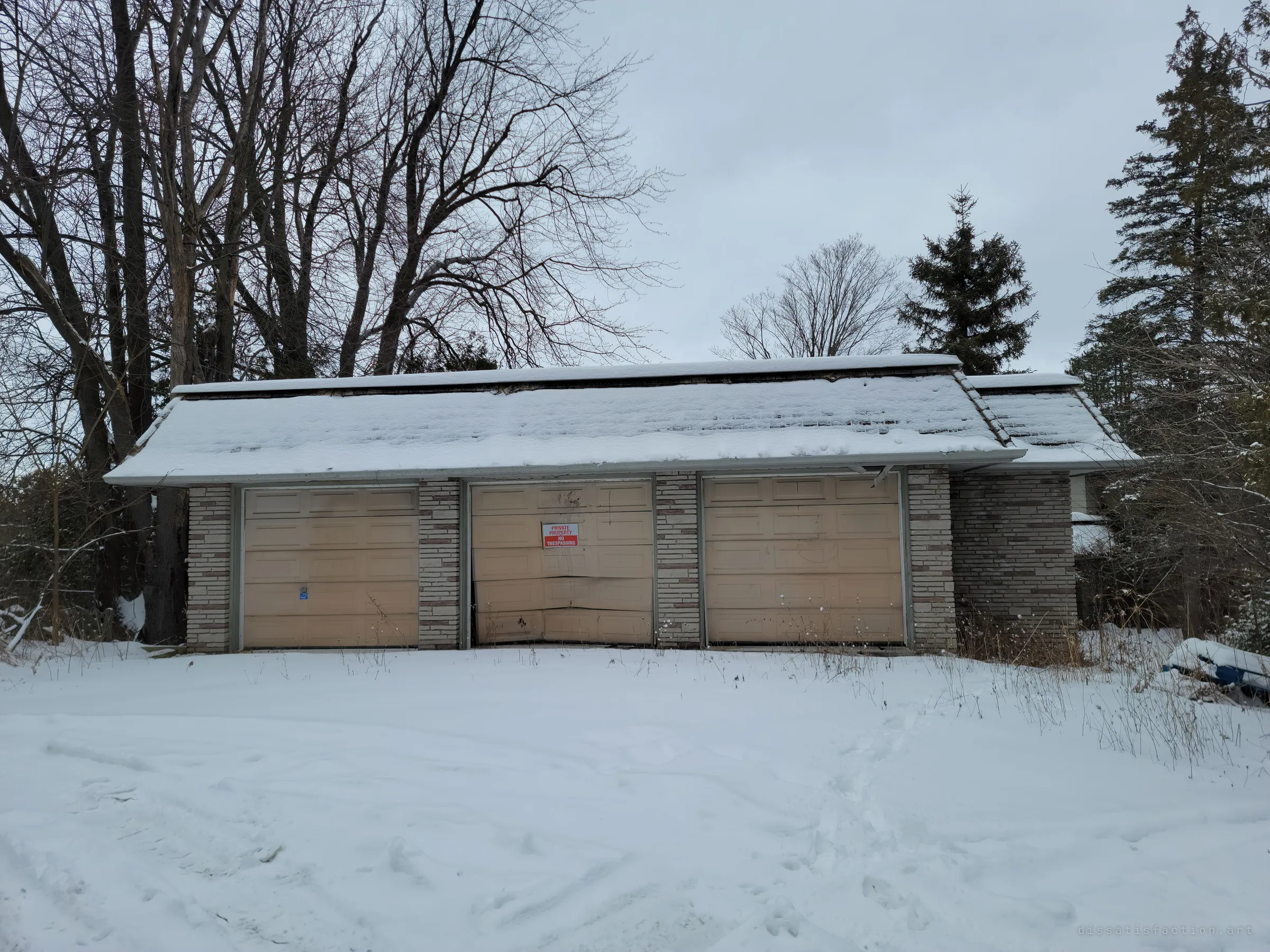 A snow-covered triple garage with stone-clad pillars, one door buckled inward and posted with a no-trespassing sign. The first look at a vacant property that has already been forced open.