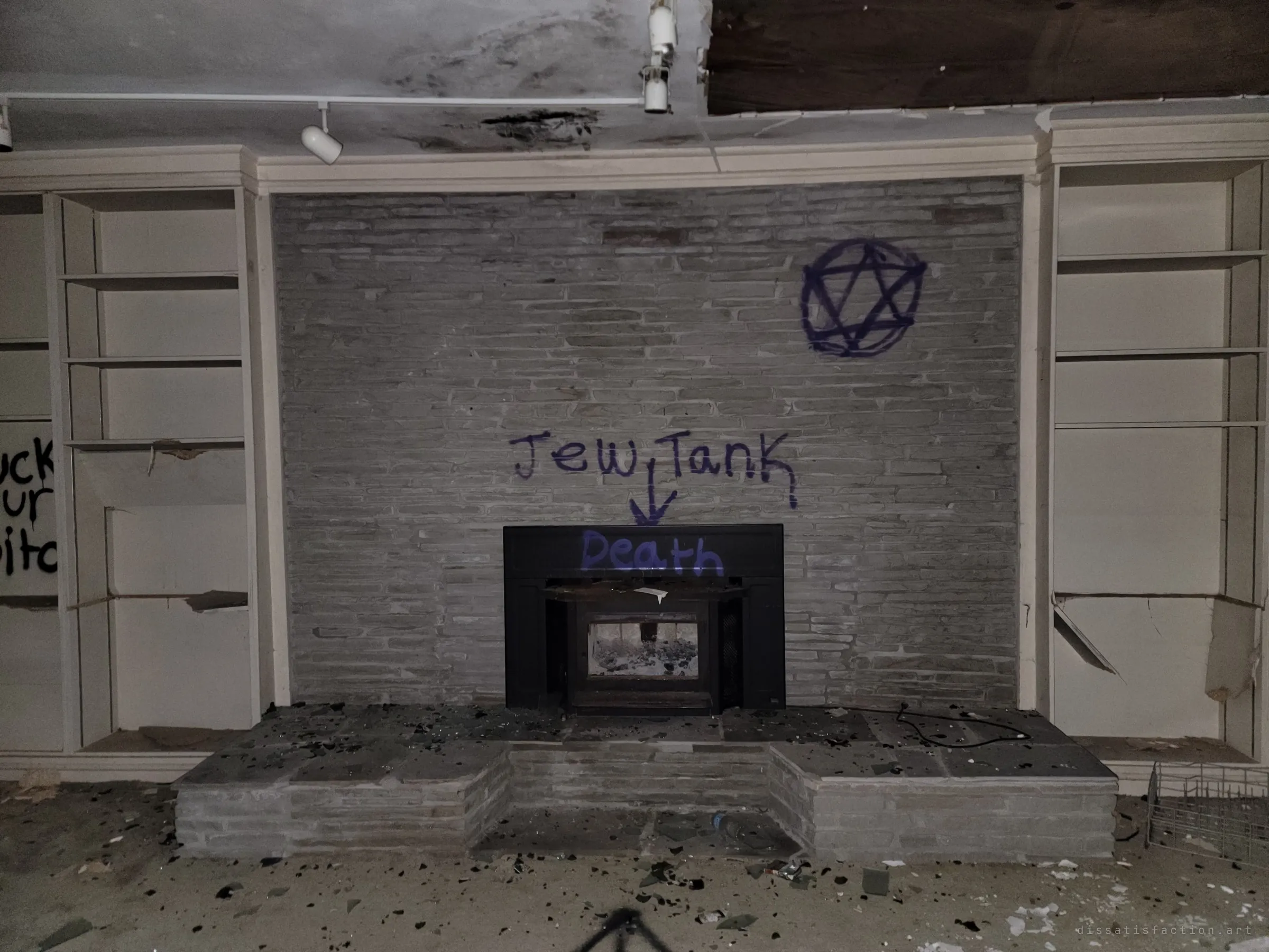 A stone fireplace between gutted bookshelves, its hearth covered in broken glass and its wall sprayed with occult symbols and hateful slogans. The vandalism has turned the heart of the living room into a threat.