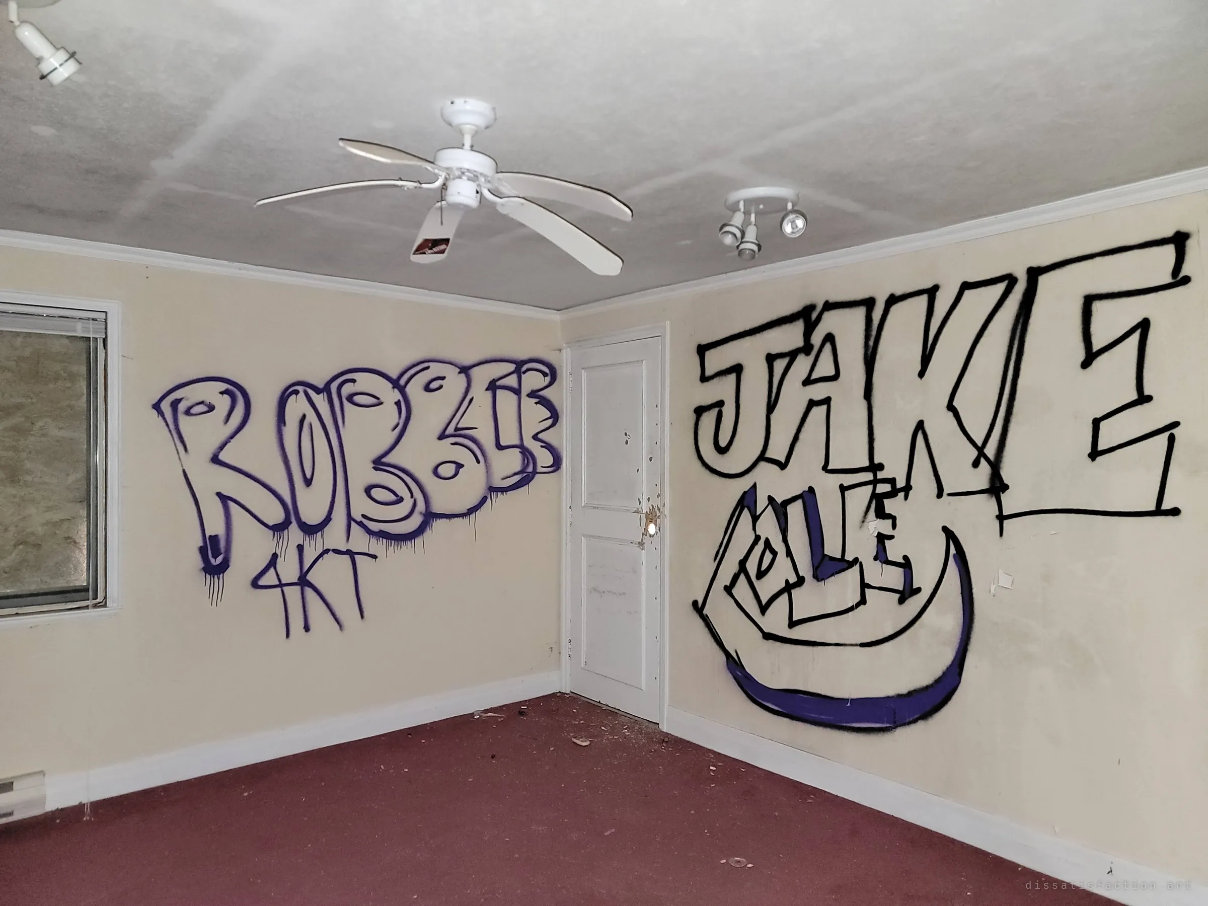 A bedroom with a ceiling fan and track lights, its walls covered in large spray-painted tags. The fresh graffiti marks how vandals have claimed the empty rooms.