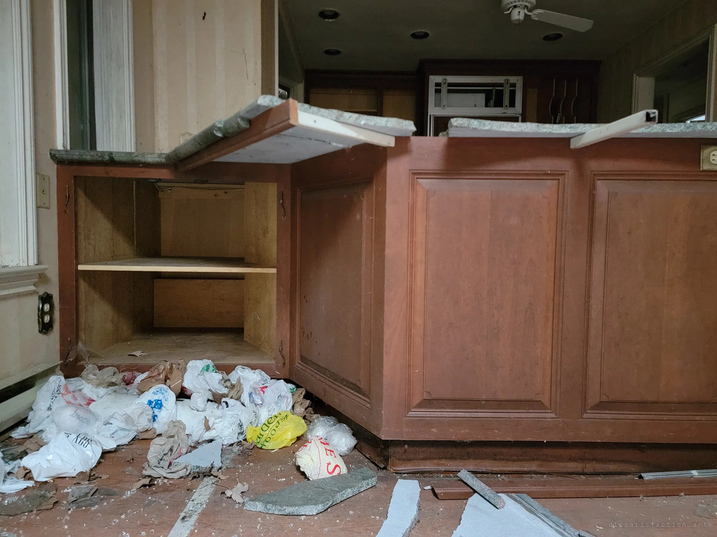 Close to the ground, the kitchen island with its countertop broken off and a heap of plastic bags beneath it. The low angle makes the wreckage loom over the frame.