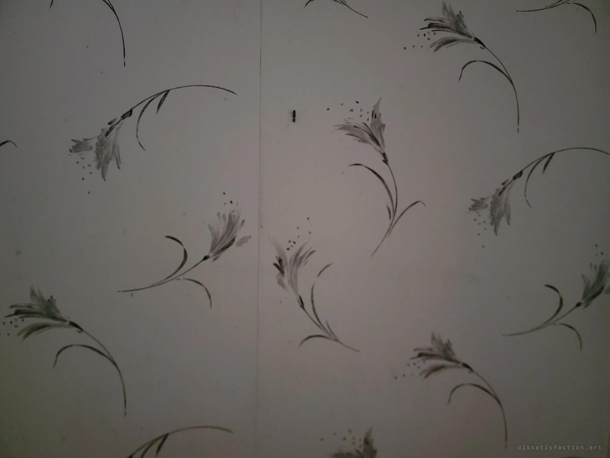 A close-up of faded wallpaper with a delicate grey hand-painted botanical pattern, split by a seam. A small detail of the original decor that survived the vandalism.