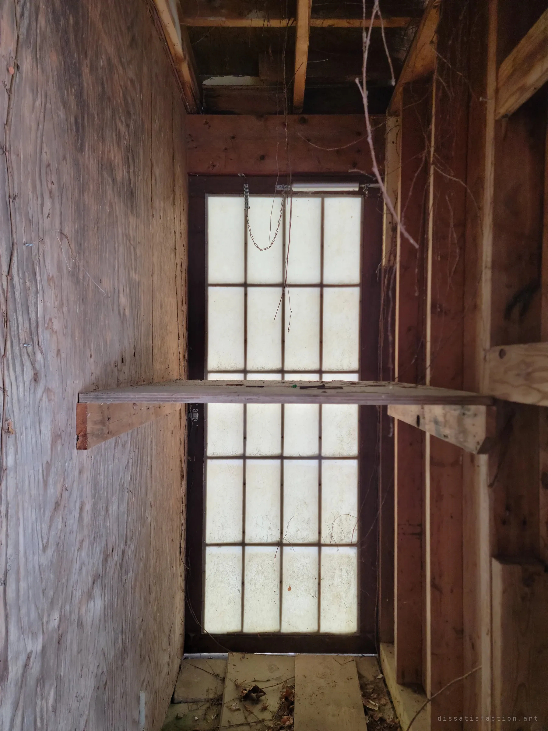 A narrow wooden alcove ending in a glowing paper-panelled door, a lone shelf cutting across the light.