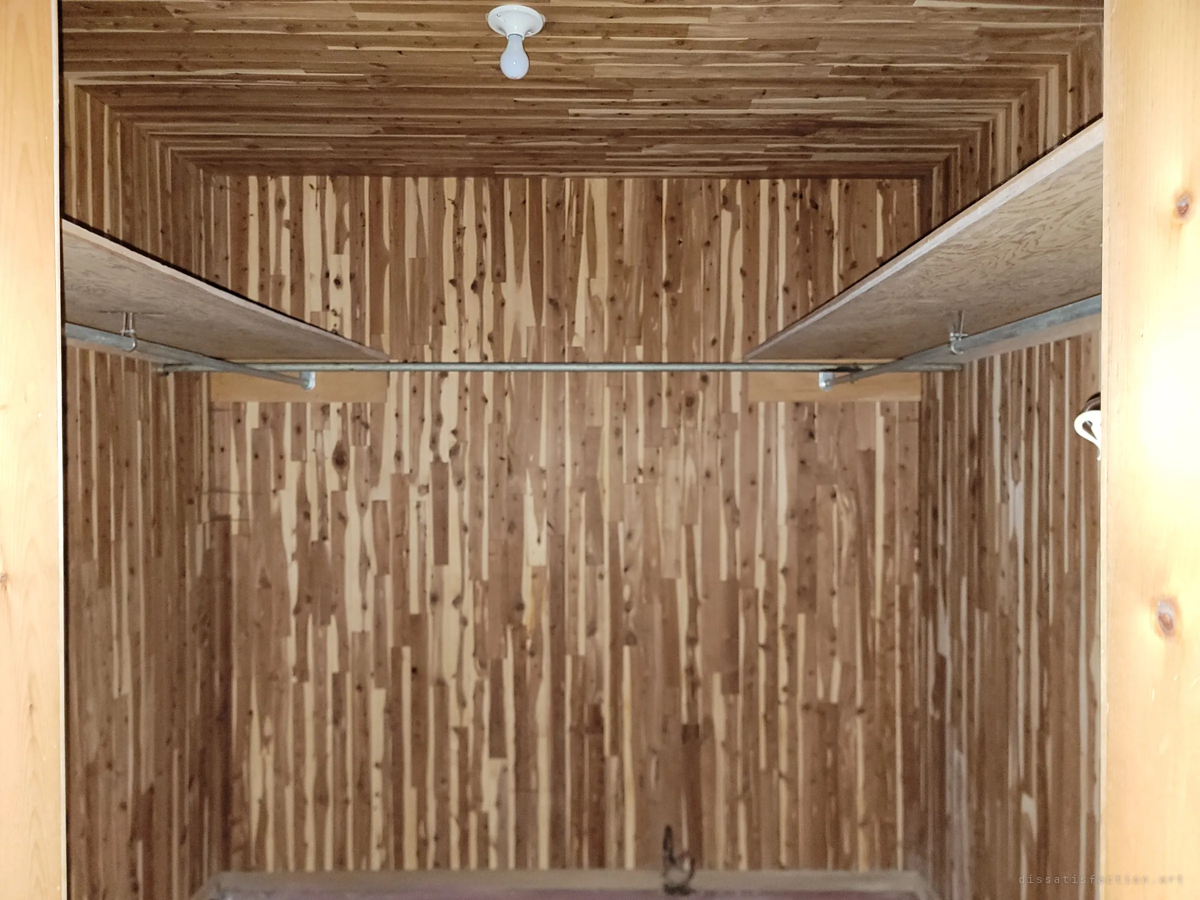 An empty walk-in closet lined floor to ceiling in cedar planks, with bare hanging rails. One of the few spaces left almost untouched.