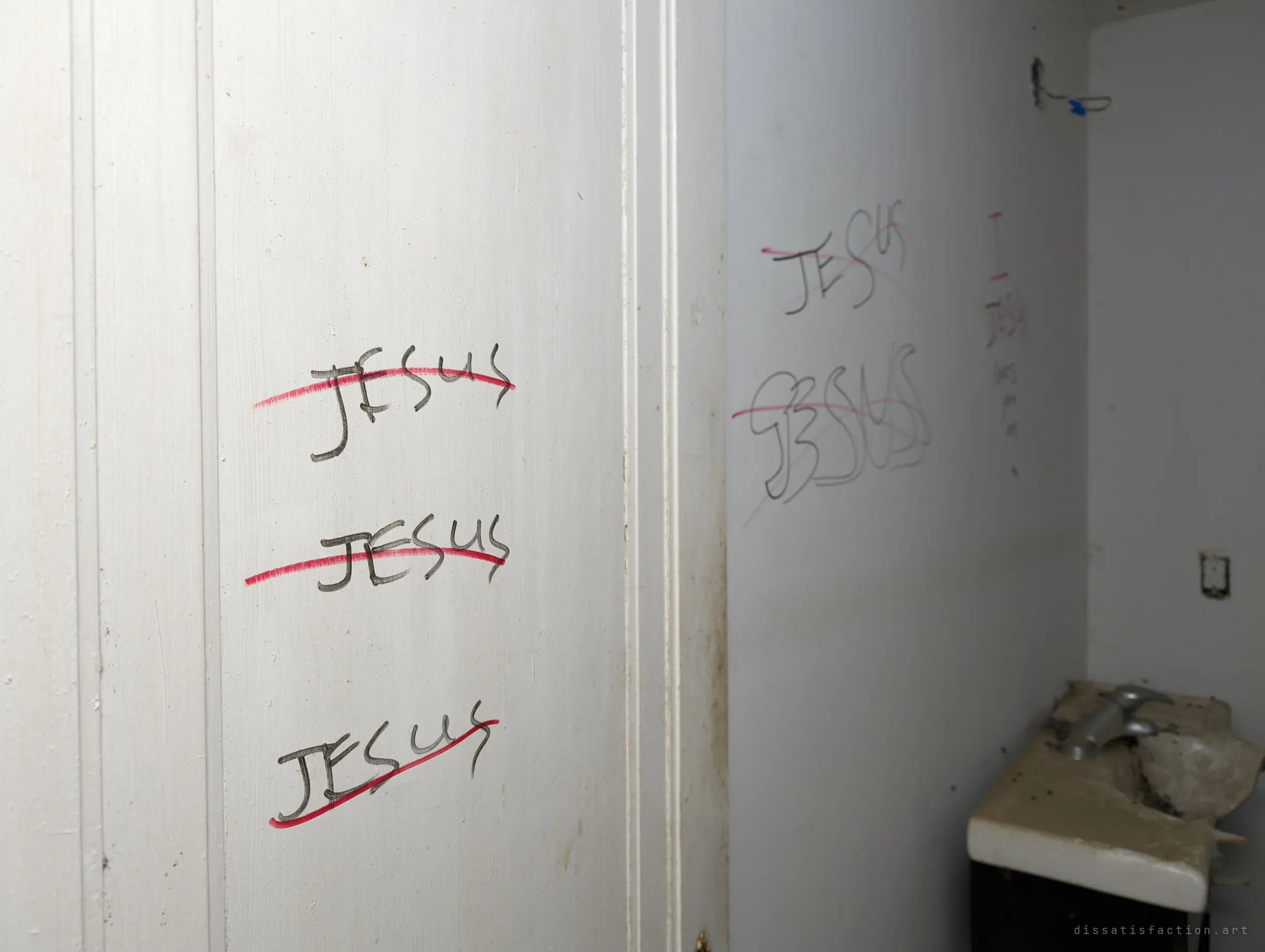 Close view of a white door frame and bathroom wall repeating the same written name again and again, each struck through in red, with a broken sink in the corner. The repetition feels like a compulsion frozen in place.