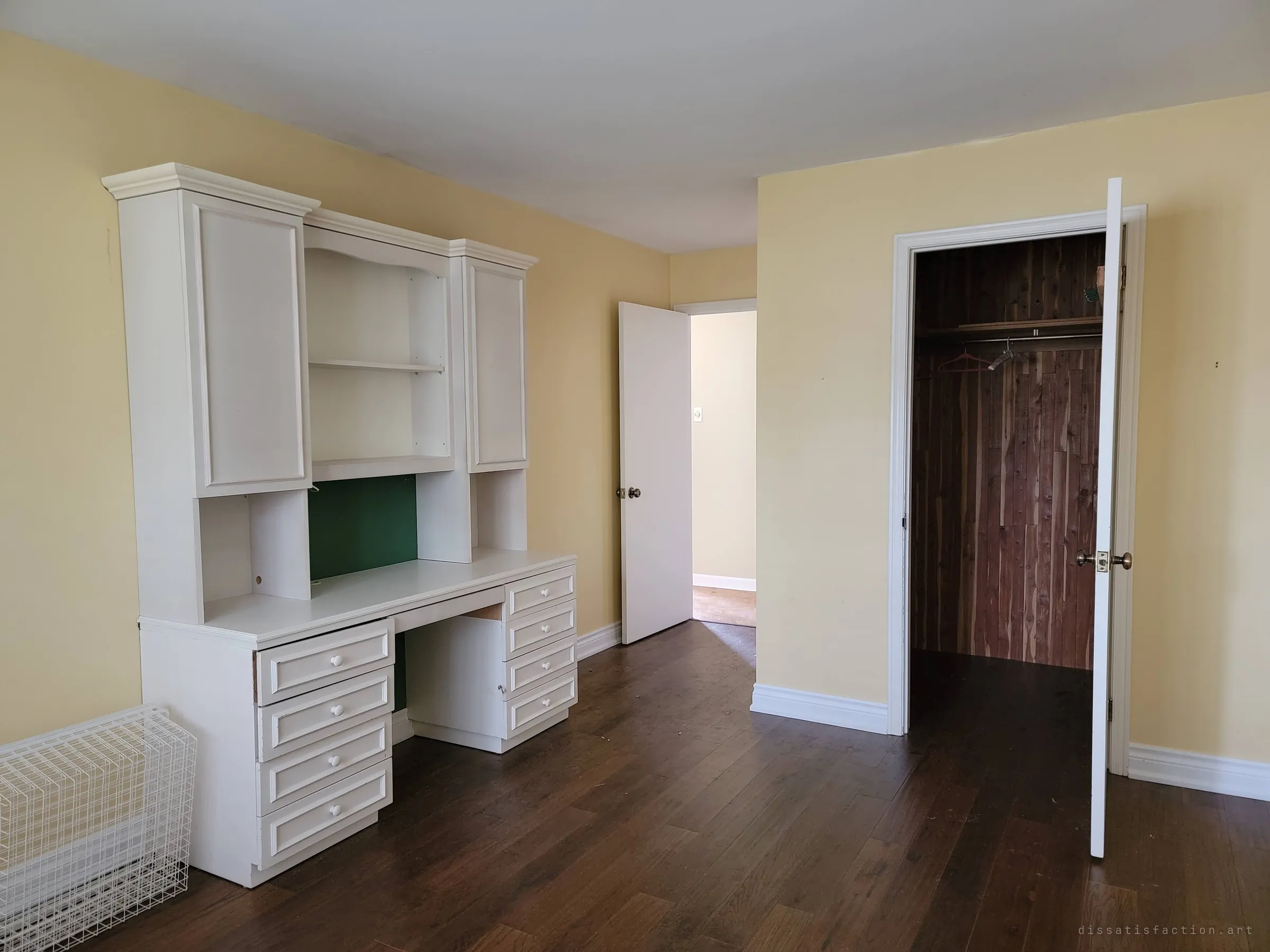 A bedroom with a built-in white desk and hutch, yellow walls and a cedar-lined walk-in closet with a few hangers left on the rail. Tidy and empty, as if the family just stepped out.