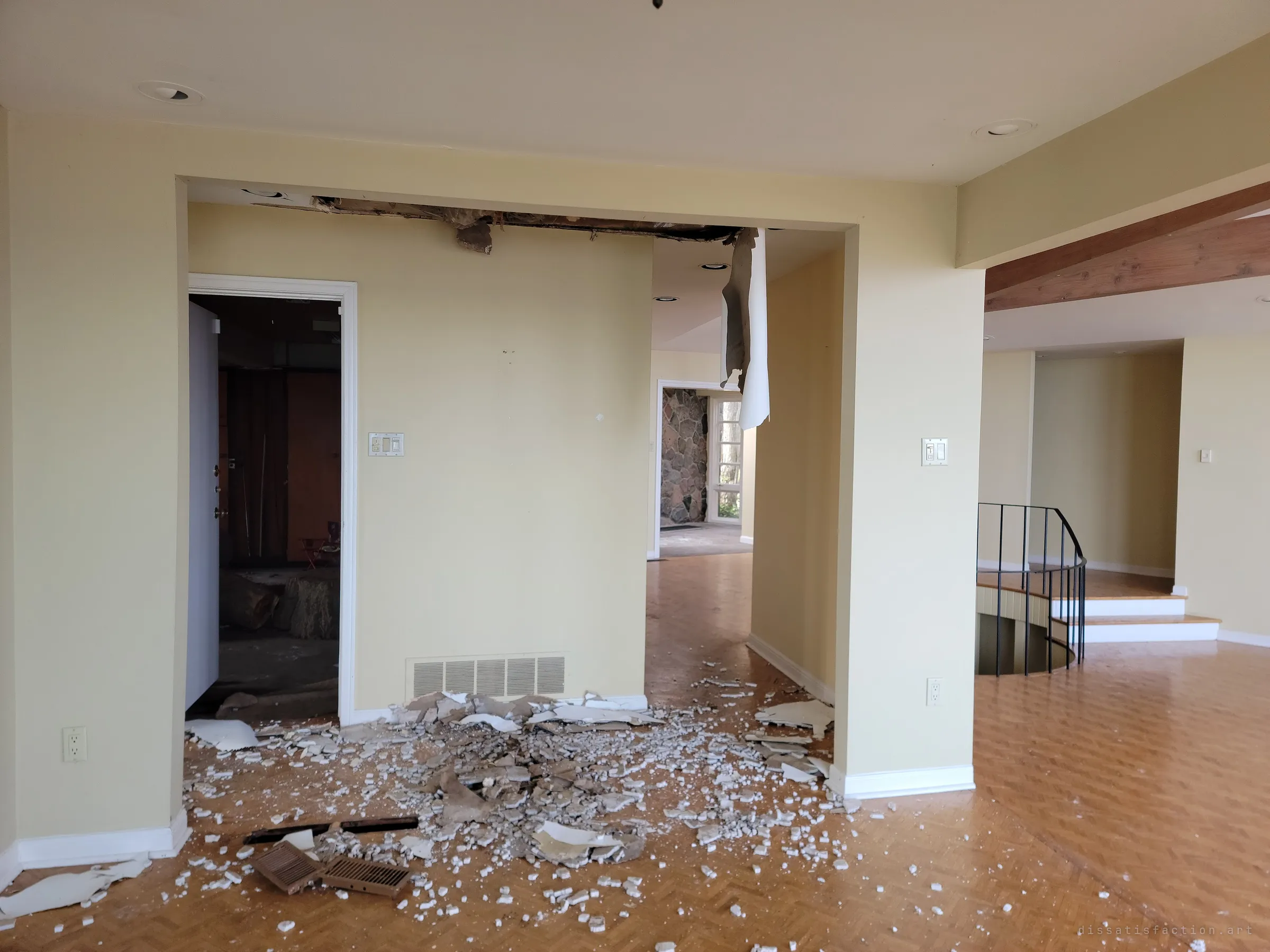 A collapsed ceiling has dumped plaster and vent covers across the parquet floor between two doorways, with a spiral stair railing off to the right. The first clear sign of water getting in.