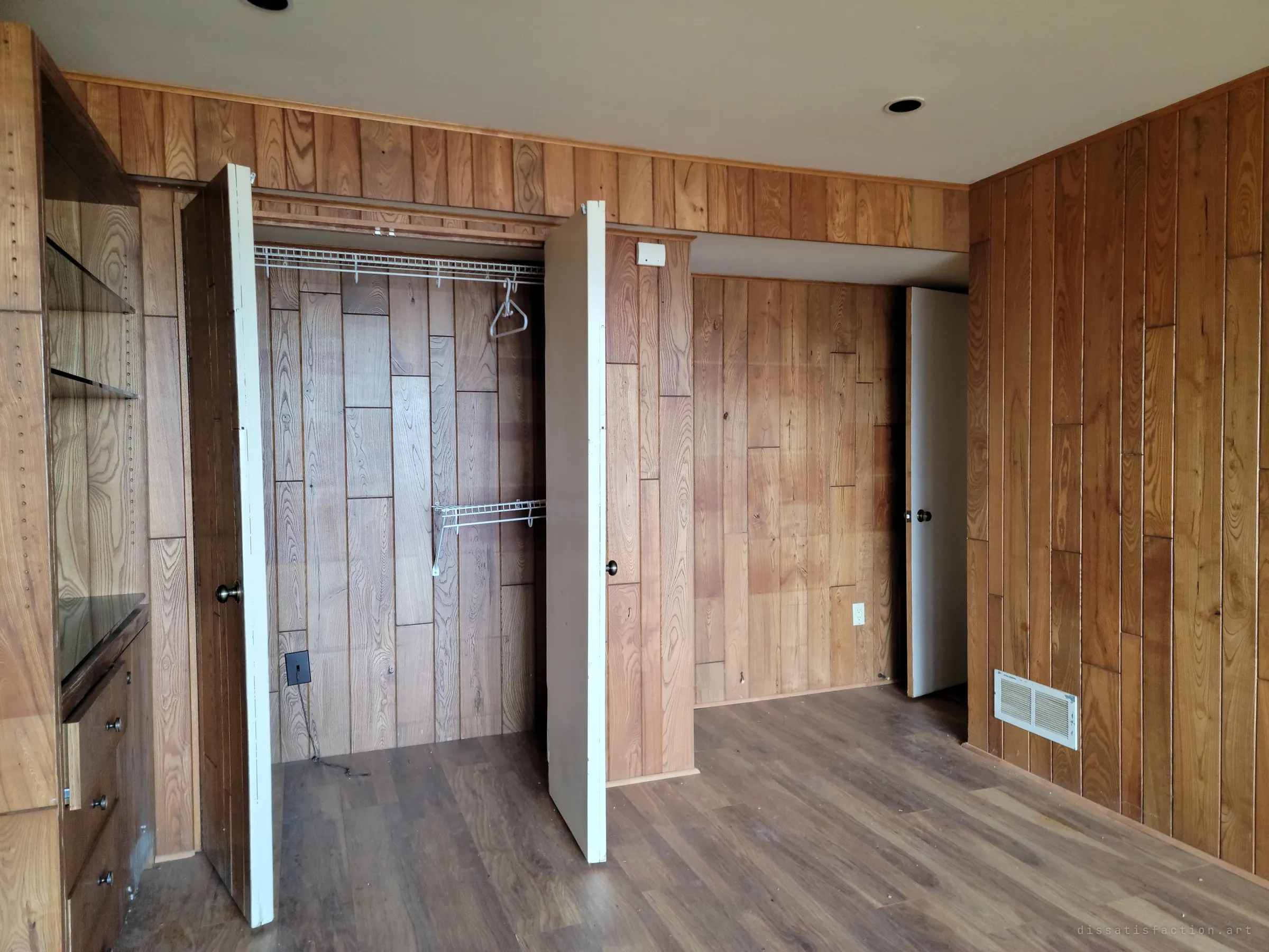 A wood-panelled bedroom with both closet doors hanging open on empty wire shelves and a single hanger. The warm grain of the panelling makes the emptiness feel recent.