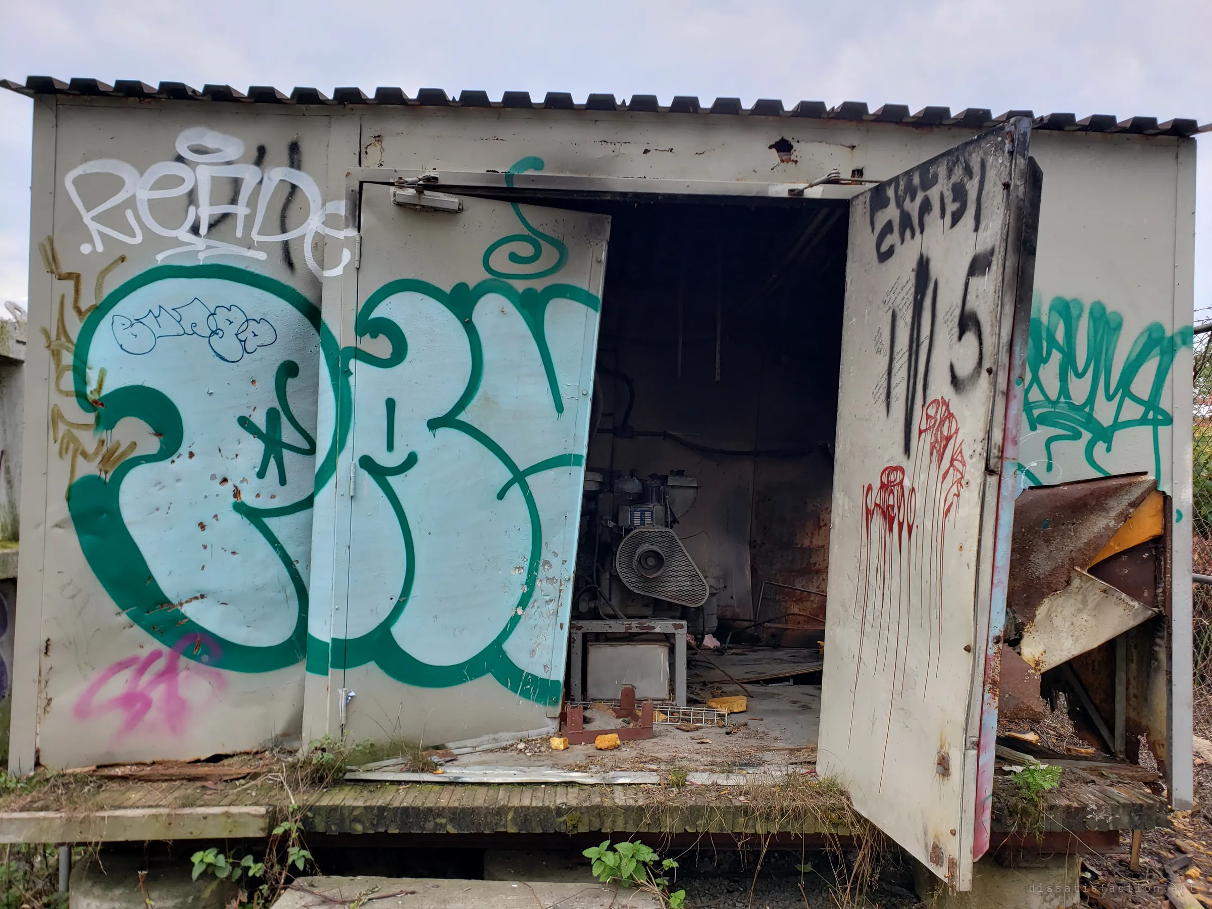 The equipment shed with its doors pried open, a big bubble-letter piece on the front and an old generator rusting in the dark inside.