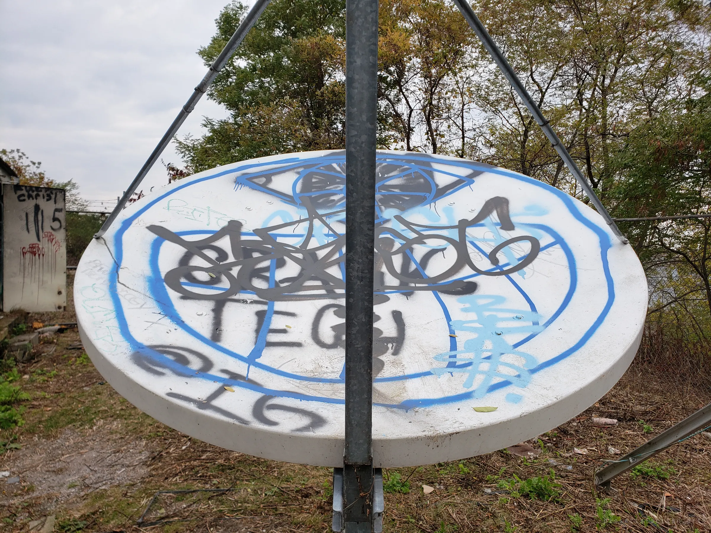 The back of the satellite dish, split by its steel mast and covered in blue and black tags, with autumn trees behind.