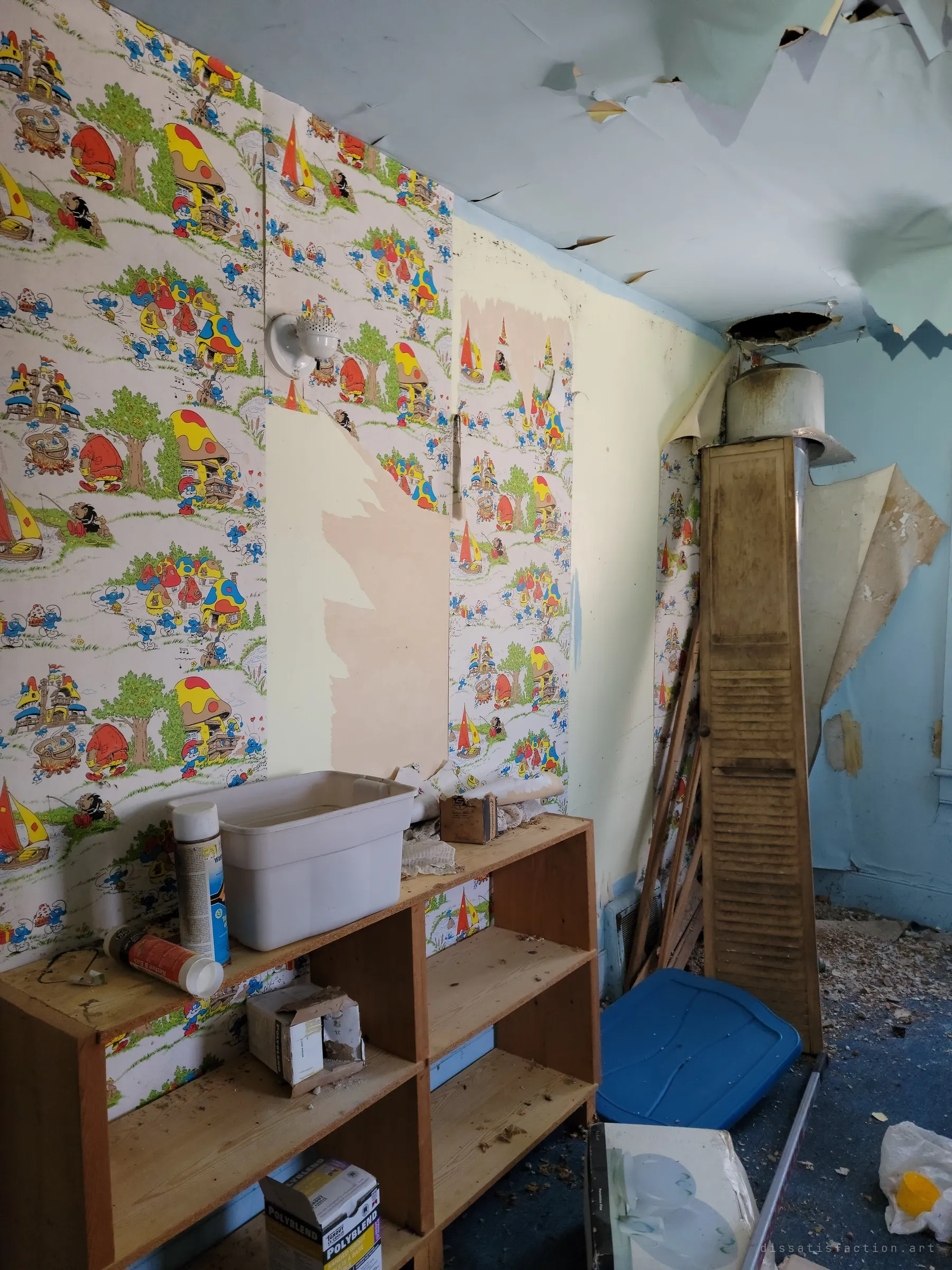 A child's room papered with cartoon village wallpaper, now peeling, beside a sagging ceiling and a bare shelf of leftover cans and boxes. The cheerful pattern against the decay is the heart of the house.