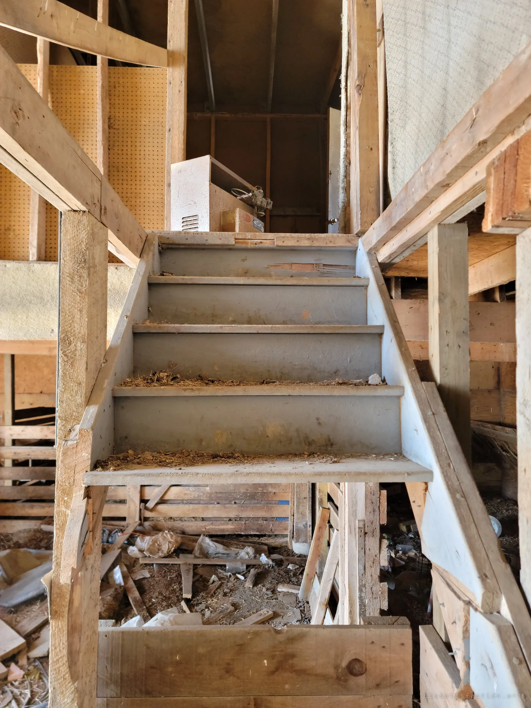 A grey-painted wooden staircase leading straight up into the barn loft, with pegboard walls and an old cabinet at the top. Debris collects on each step.