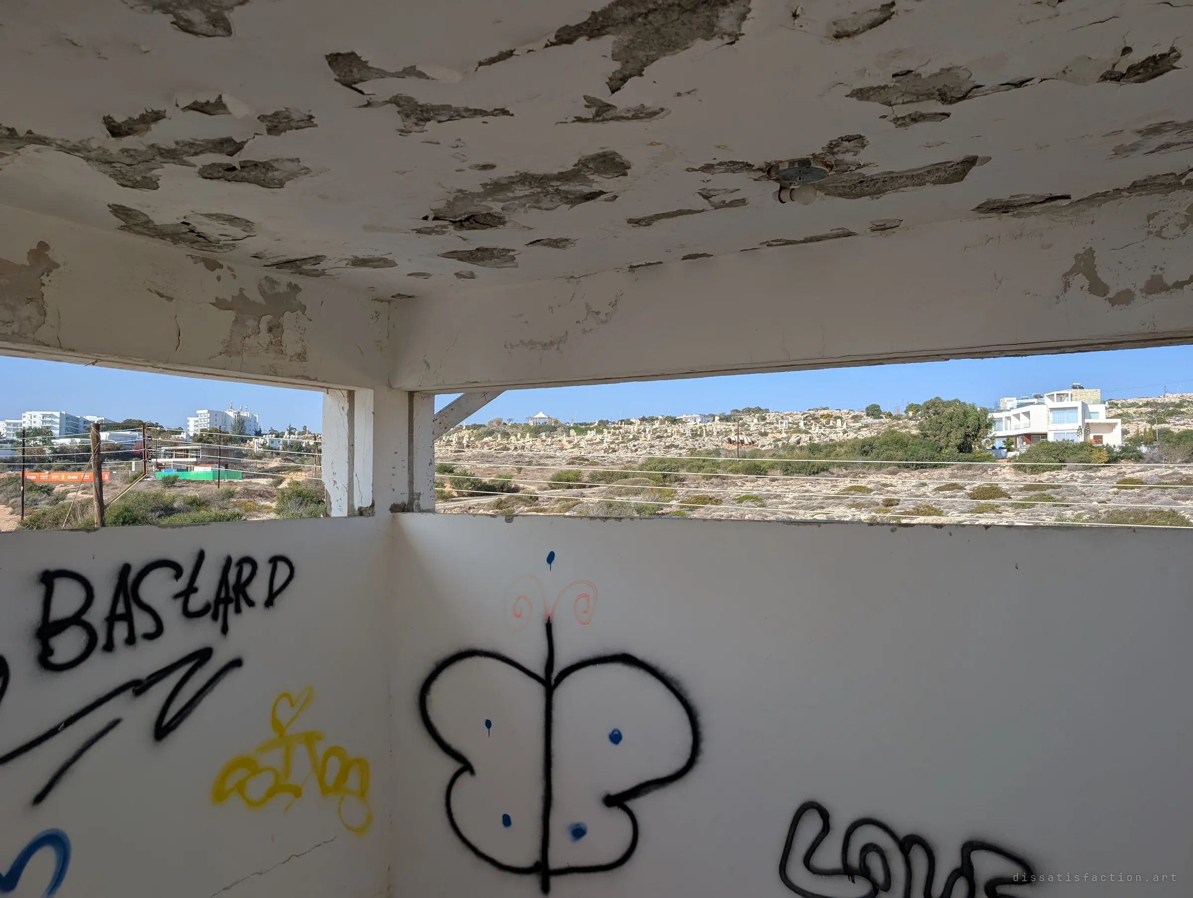 From the little rooftop lookout, graffiti-covered walls frame a strip of view over dry scrubland. The peeling ceiling and scrawled tags show how exposed the lookout has become.