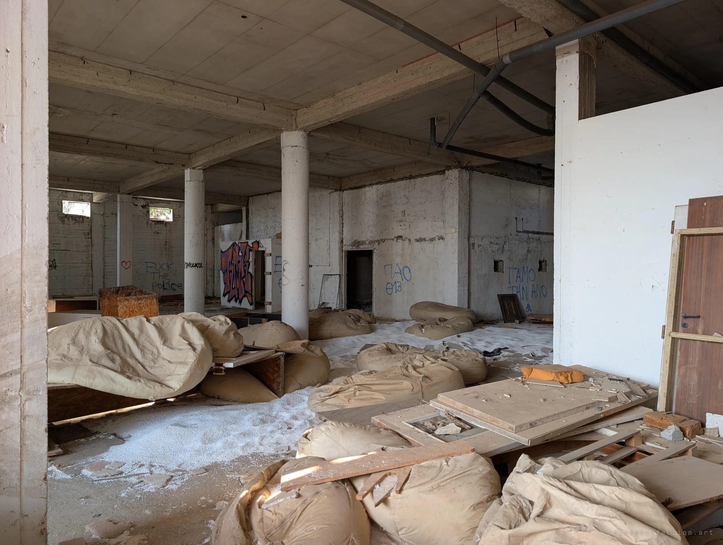 A wide concrete hall with round pillars is littered with deflated beanbags, loose boards and drifts of white foam beads. Graffiti in several languages lines the bare walls.