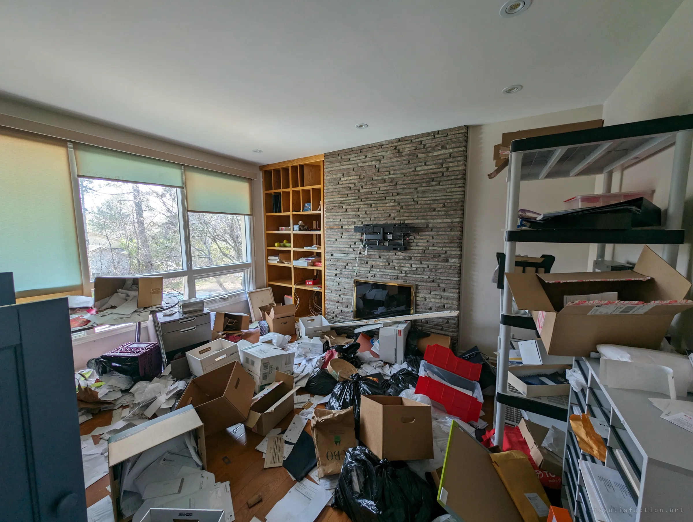 A study buried in paperwork, open boxes and garbage bags in front of a stacked-stone fireplace wall and an emptied bookcase. Someone has rifled through years of household papers and left them across the floor.