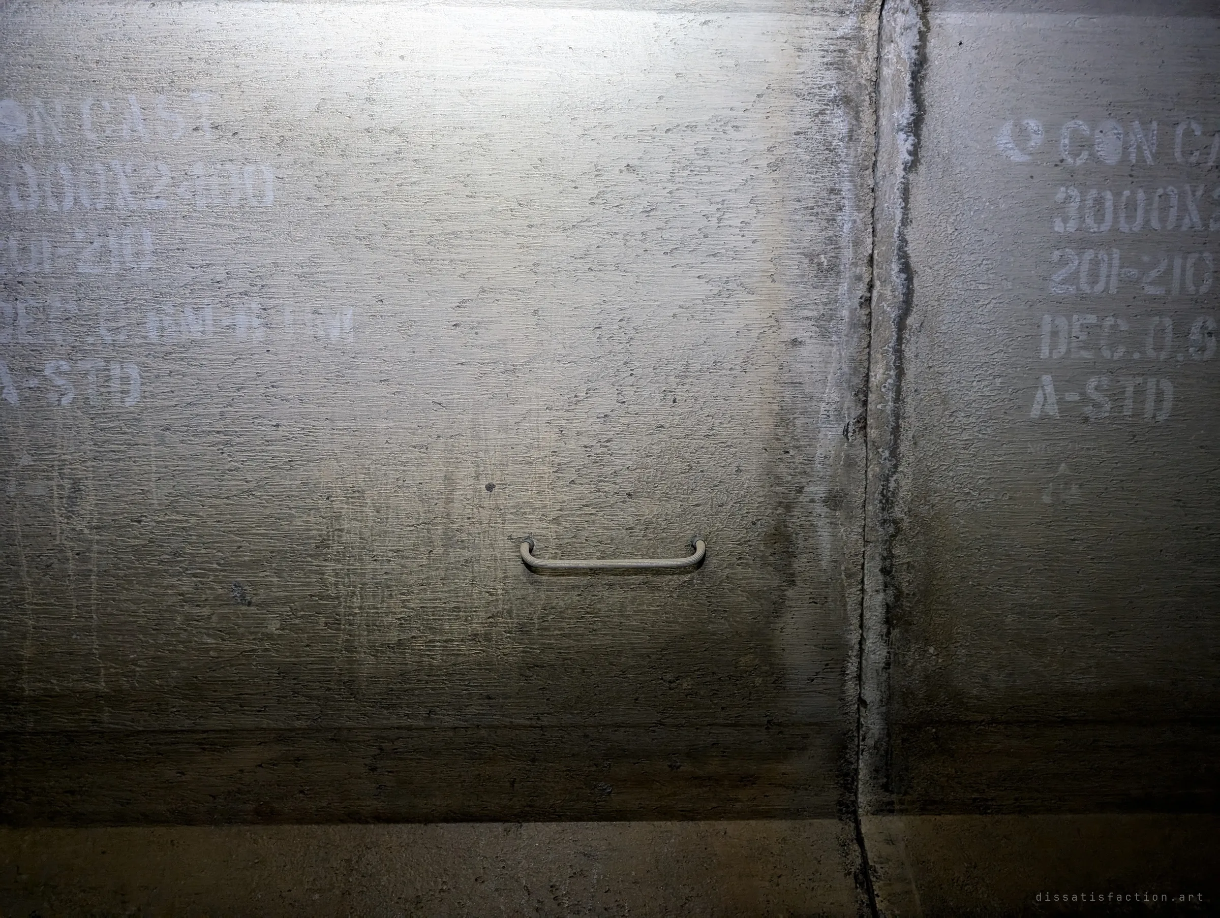 A single rung fixed in the side of a box culvert, between faded stencilled precast markings on two concrete segments. Like the others, it leads nowhere.