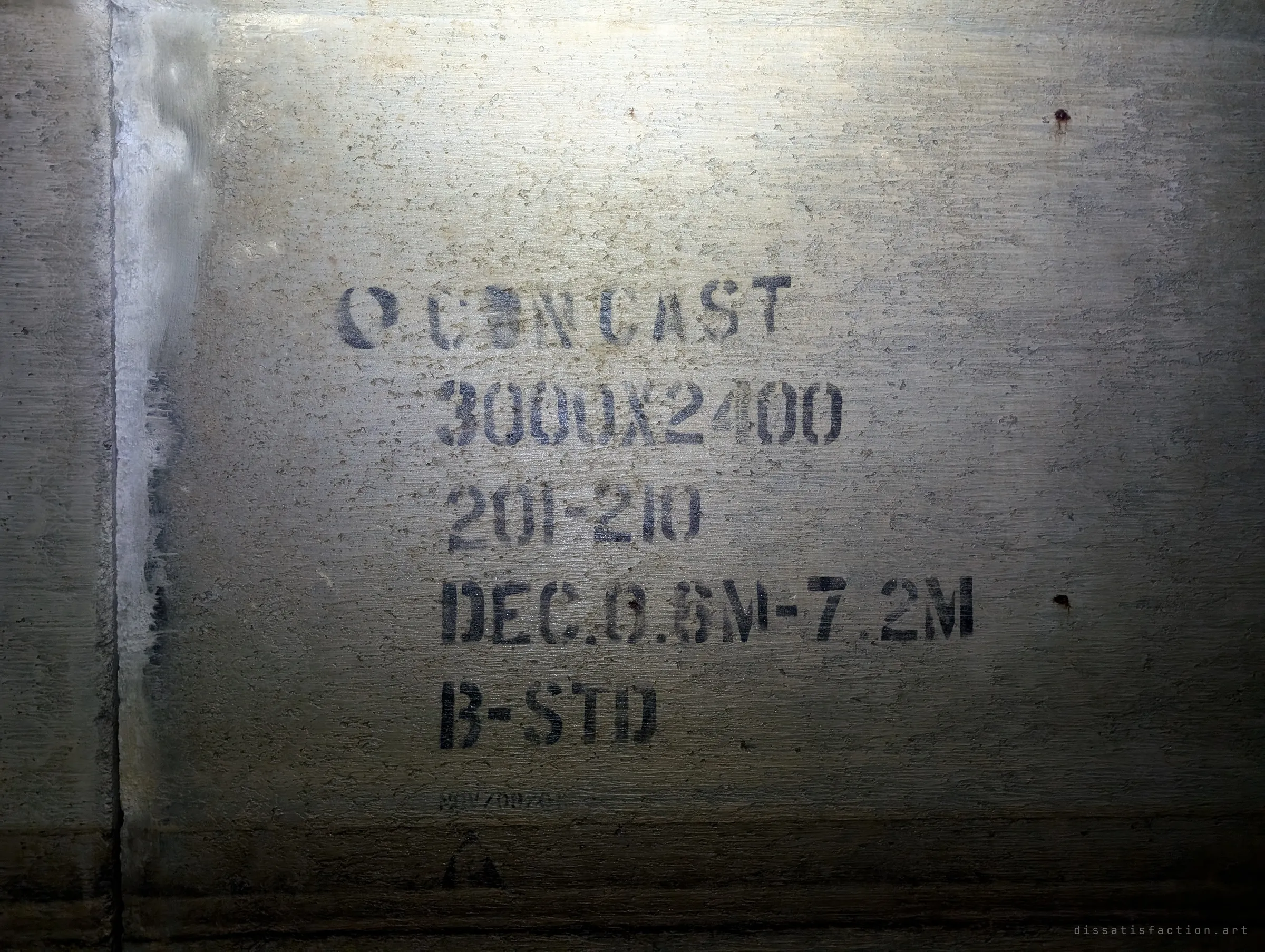 Stencilled precast maker markings with size and class codes on a culvert segment beside a joint. A close-up of the concrete the tunnel is built from.