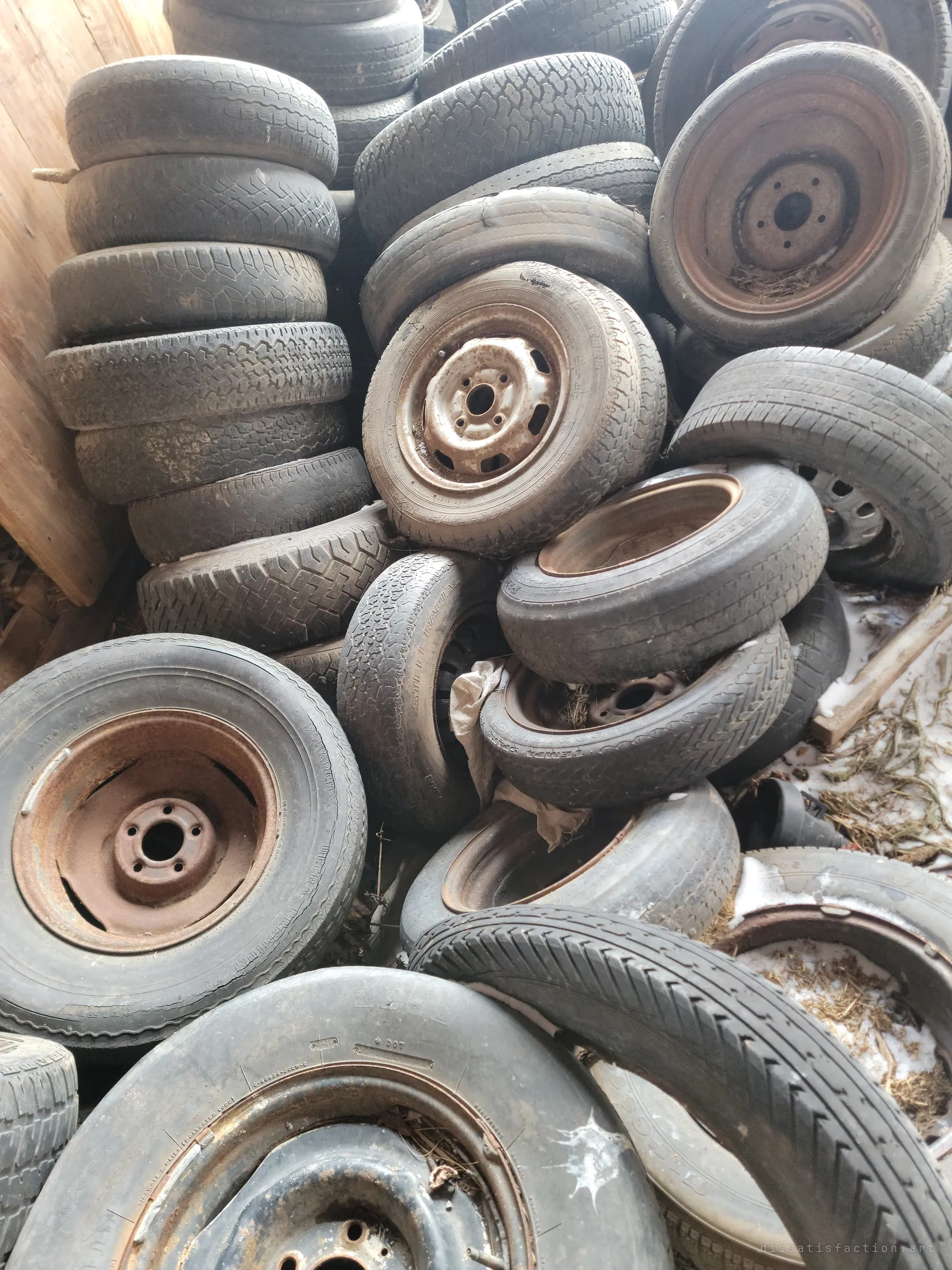 A heap of old tires, many still on rusted steel rims, piled high inside the barn. Decades of cars left their wheels behind here.