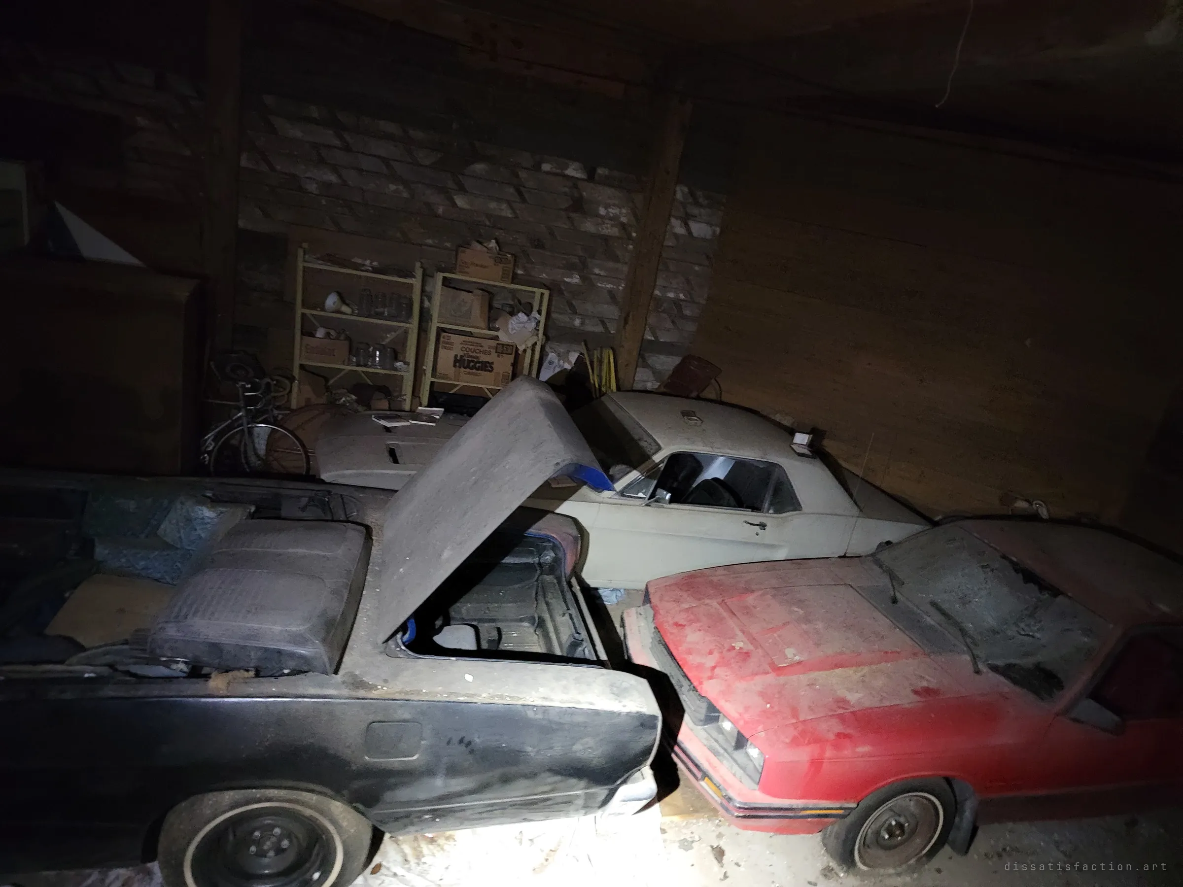 Three cars crowd one barn bay: the open black convertible, a cream classic coupe behind it and a faded red hatchback nosed in beside. Together they show how densely the collection was packed away.
