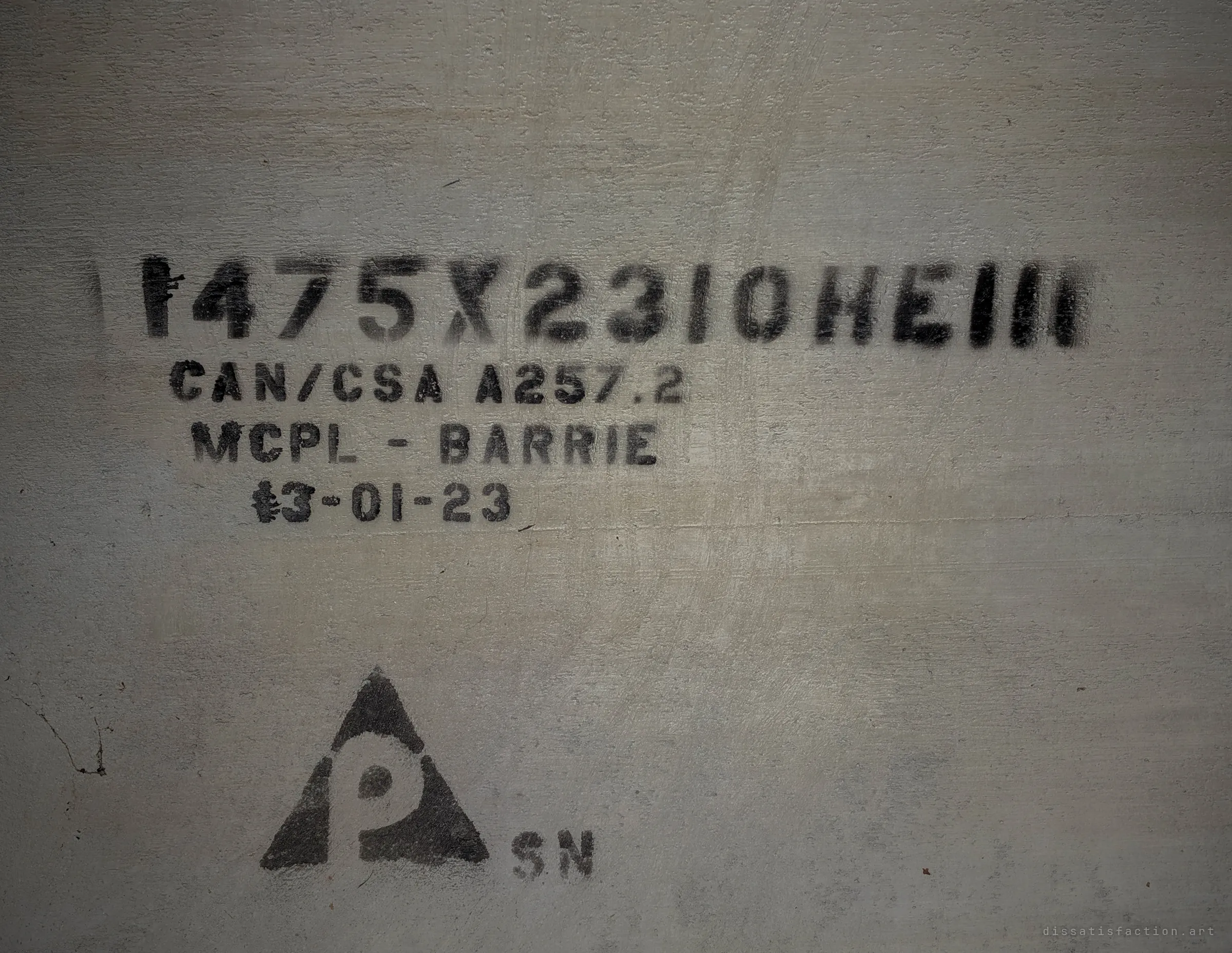 Close-up of stencilled manufacturing marks on a concrete pipe: size code, a standards reference, a production date and a maker's triangle logo. Generic pipe markings that date this section of the system.