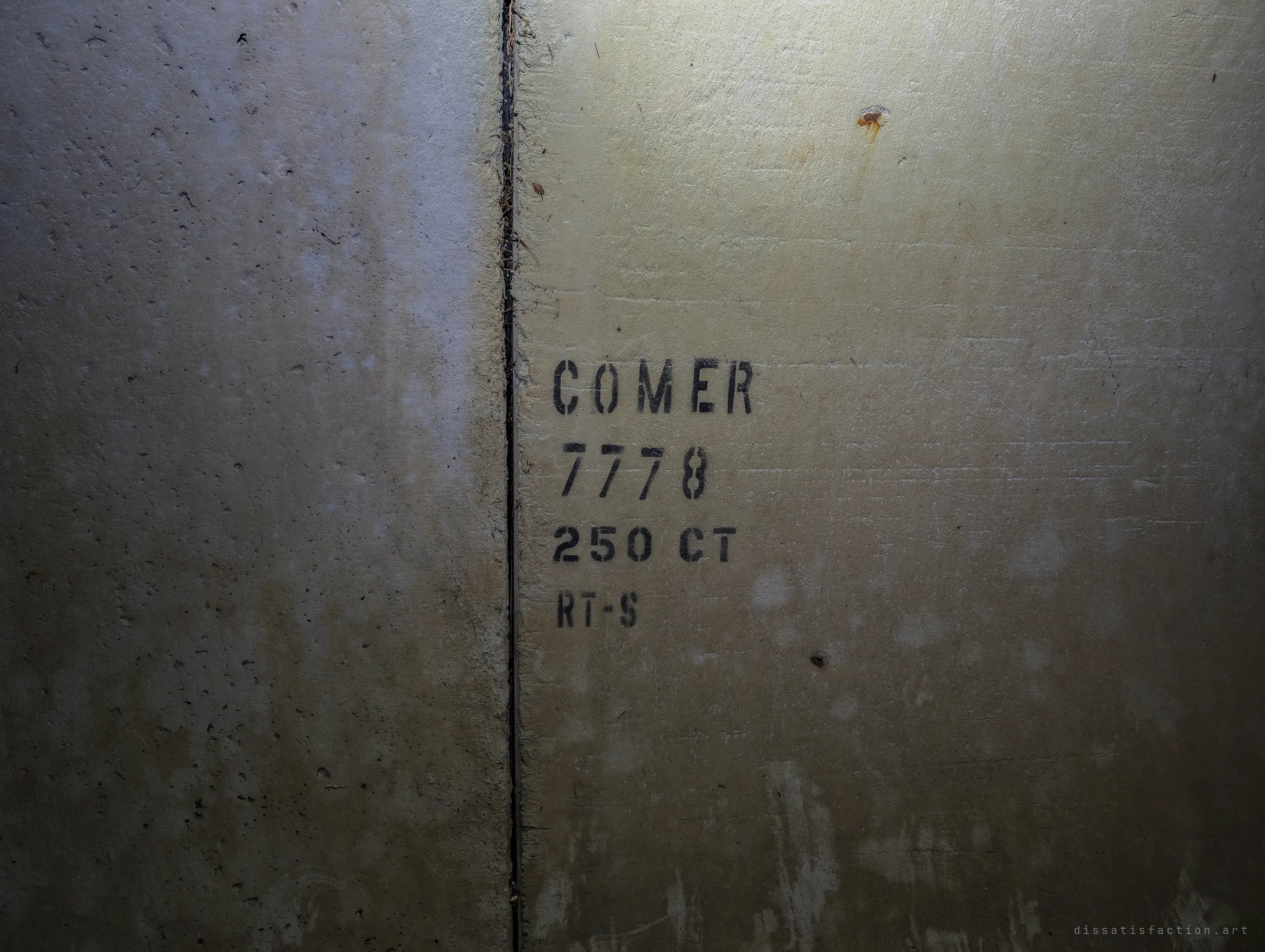 A stencilled production code on a precast concrete wall next to a vertical joint, lit by a warm flashlight glow. A small detail of how the structure was assembled from factory-made pieces.
