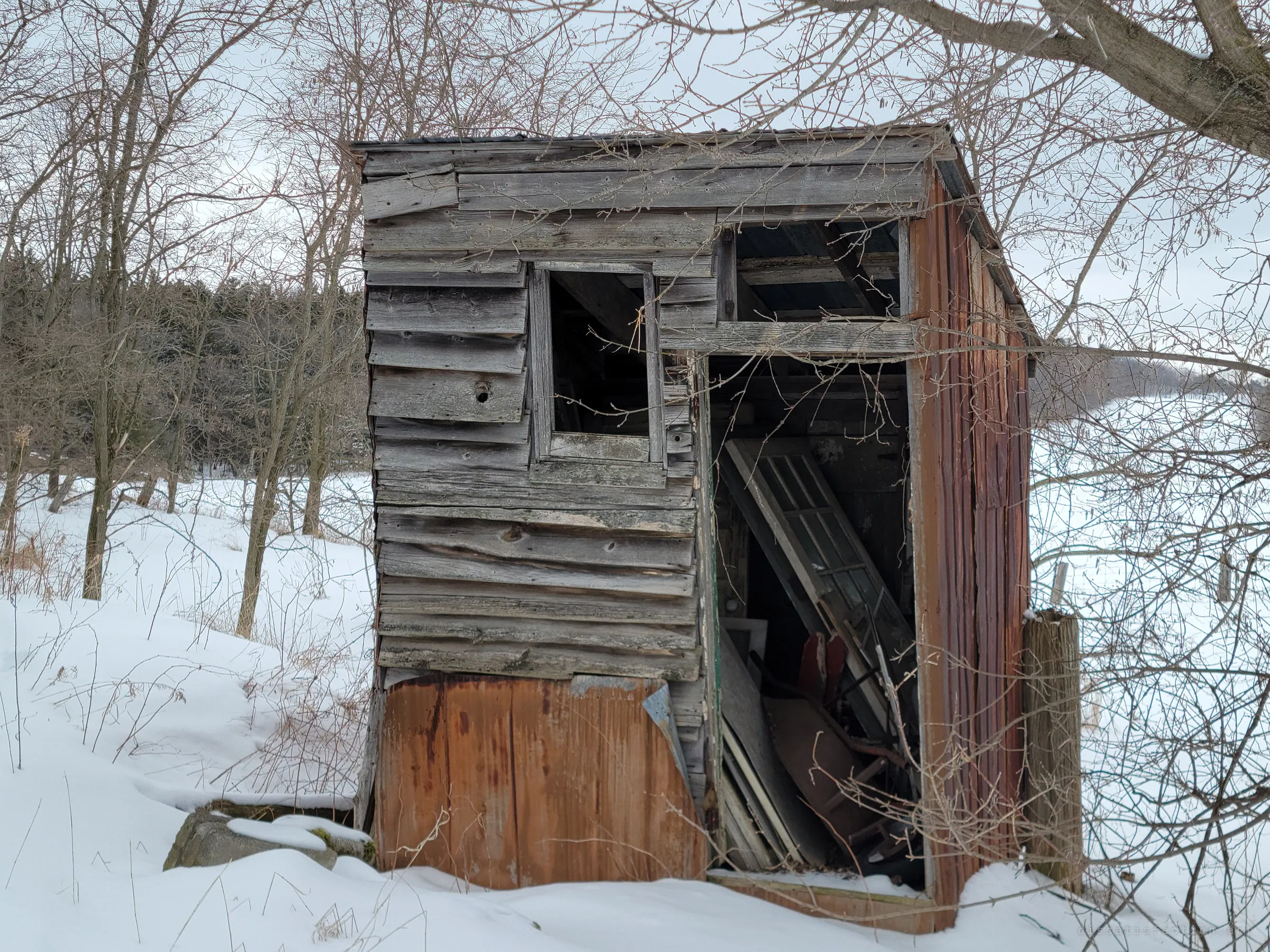 A leaning weathered shed of grey boards and rusted sheet metal, its doorway crammed with old windows and scrap. Even the smallest building on the property is full.