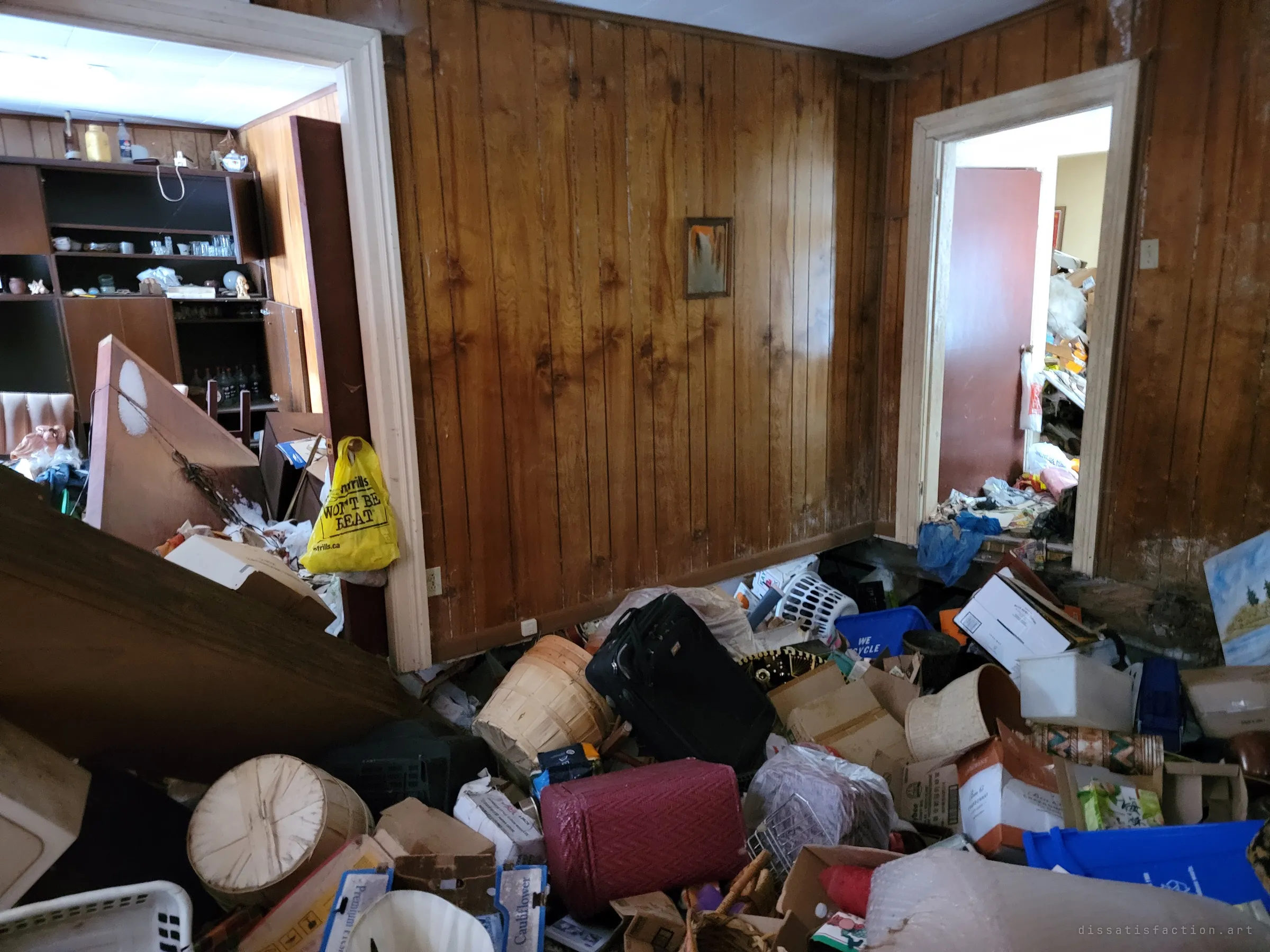 A panelled room filled waist-deep with suitcases, boxes and bins, doorways opening onto more clutter beyond. It shows the full scale of the hoard.