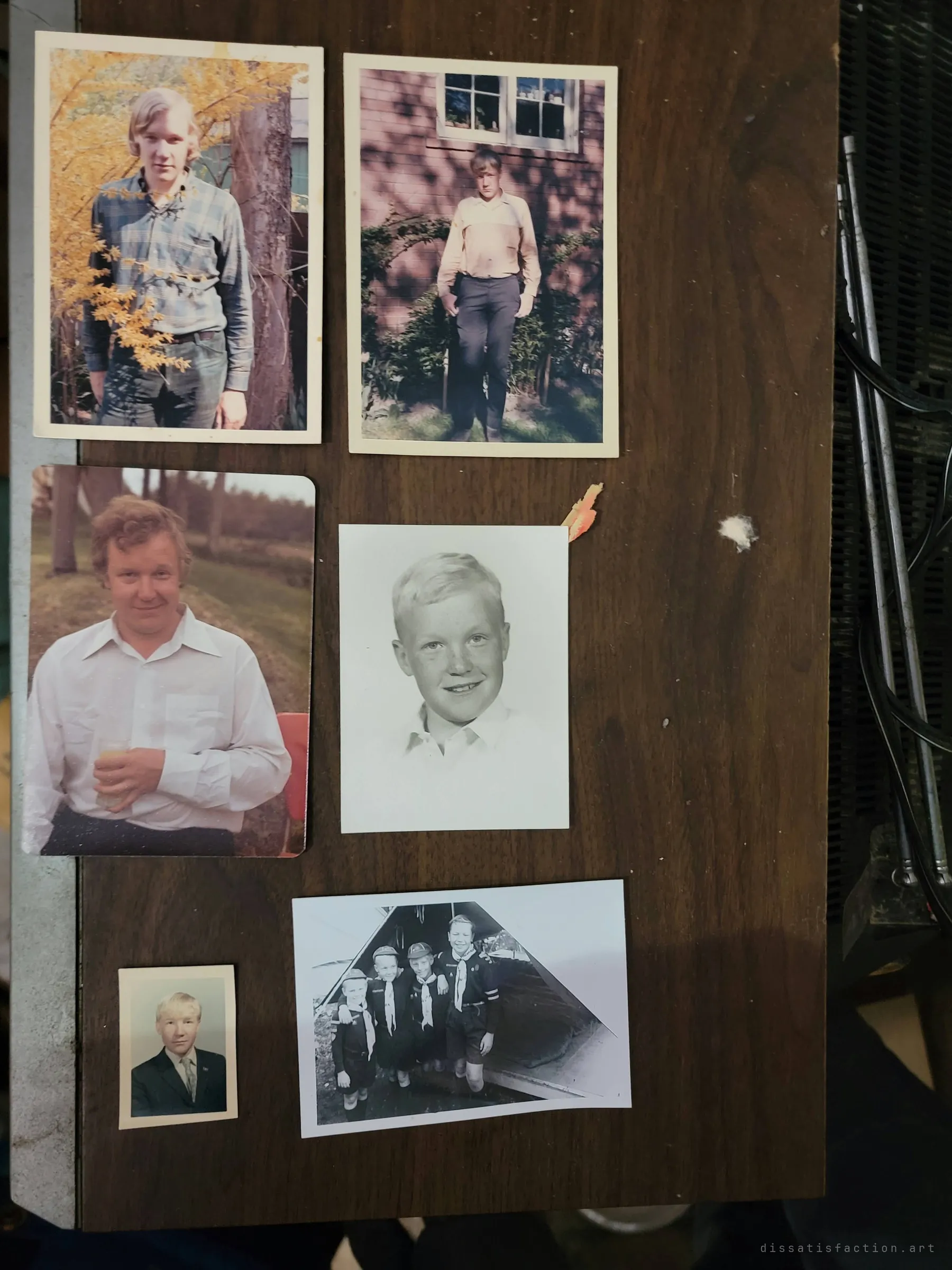 Six old family photos laid out on a wooden table: a young man in several eras, school portraits and a group of boy scouts. The owner's life story, left behind in the house.