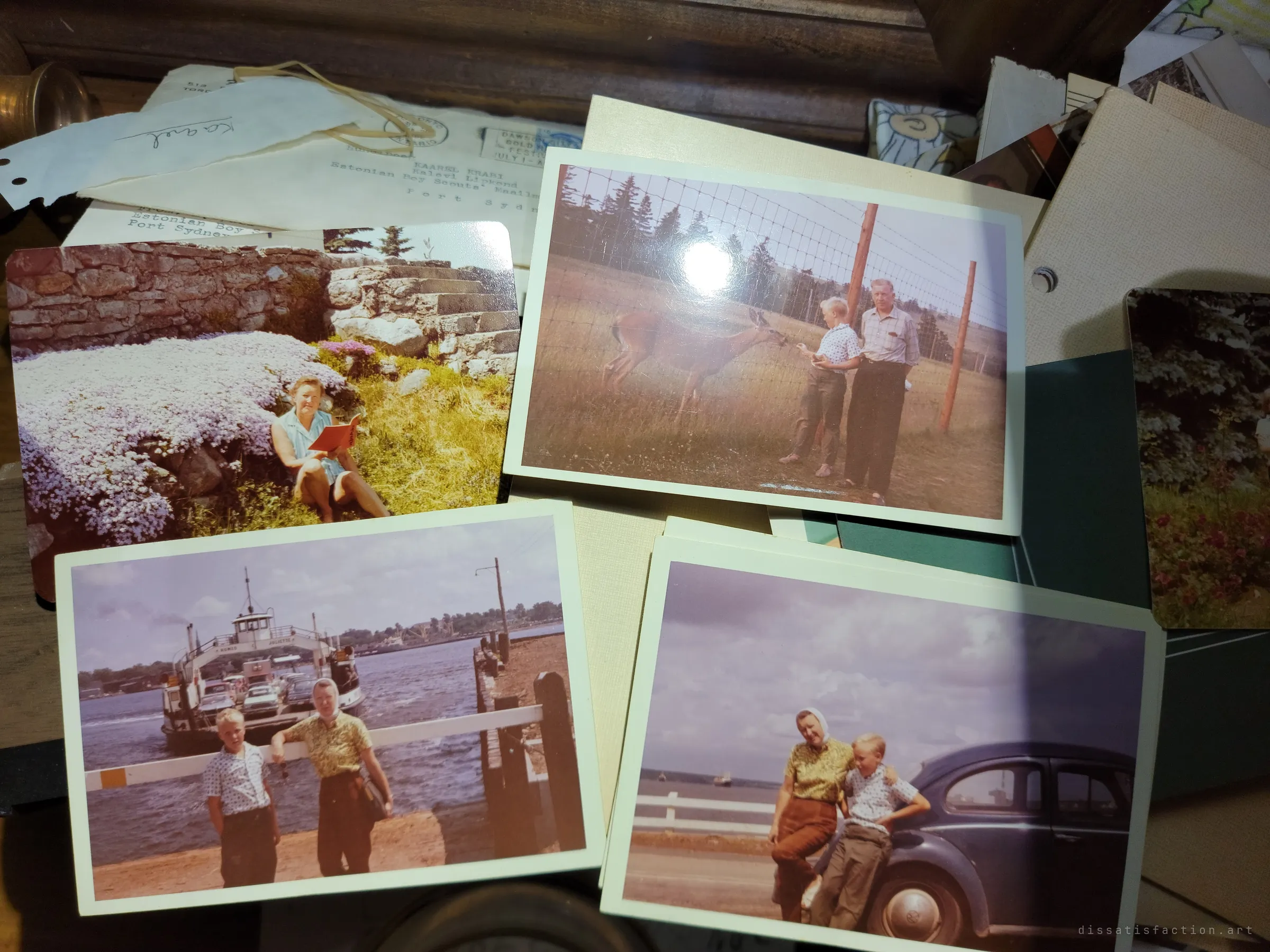 Vintage colour snapshots of a family on holiday, by a ferry, feeding a deer and leaning on an old car, spread over a pile of old letters. A family history scattered through the house.