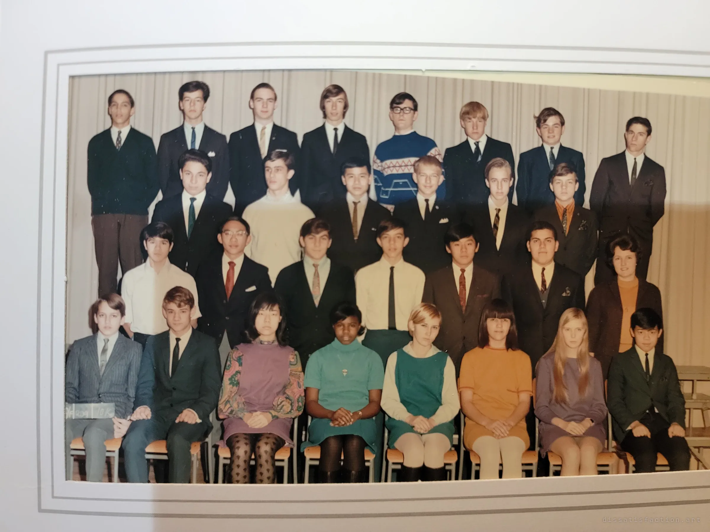 A framed colour class photograph from the late 1960s: four rows of teenagers in suits, sweaters and bright dresses with their teacher, found among the owner's keepsakes.