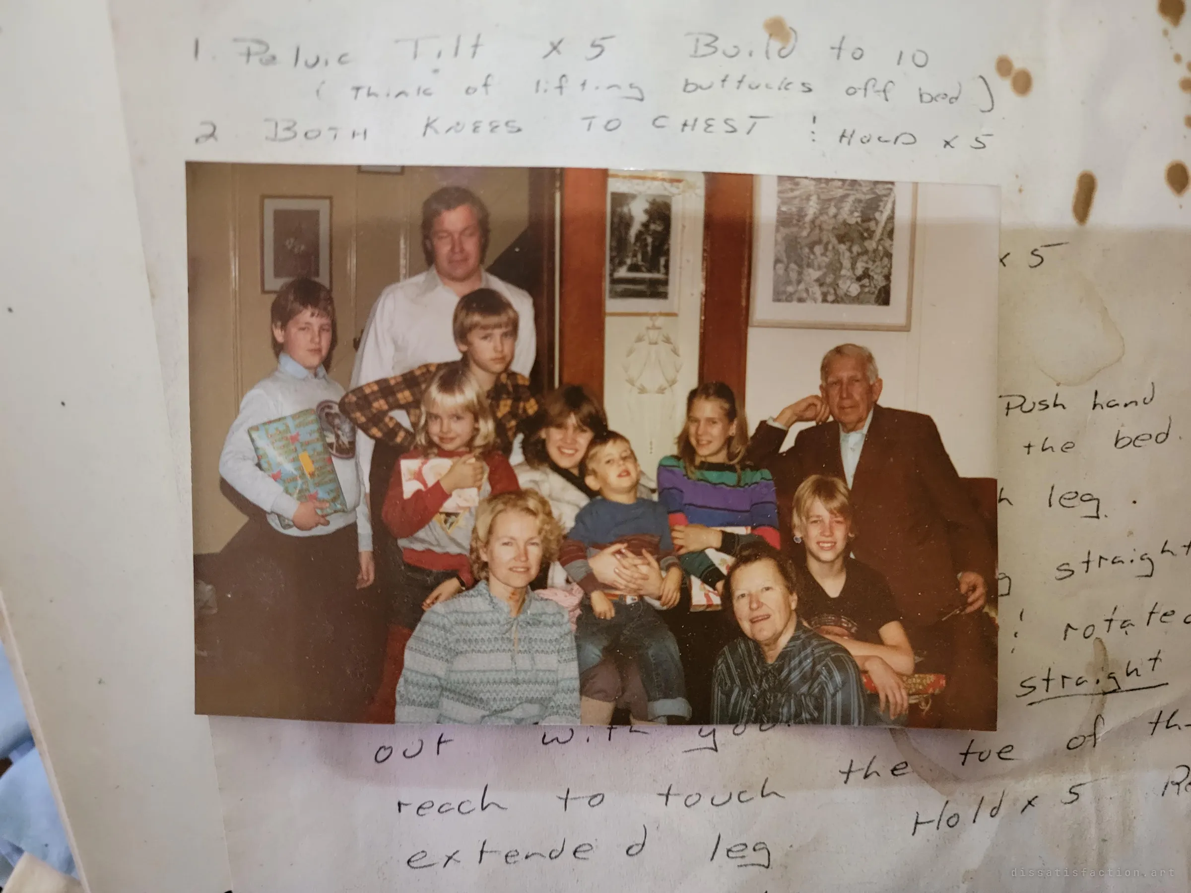 An old family snapshot of three generations crowded around a couch with wrapped presents, lying on a sheet of handwritten physiotherapy exercises.