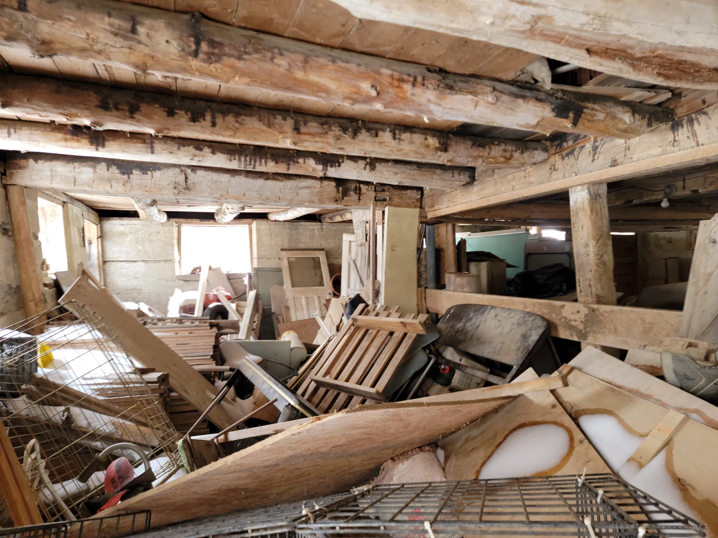 A low basement under hand-hewn log beams, choked with collapsed plywood, crates, doors and wire shelving, snow drifted in through the gaps.