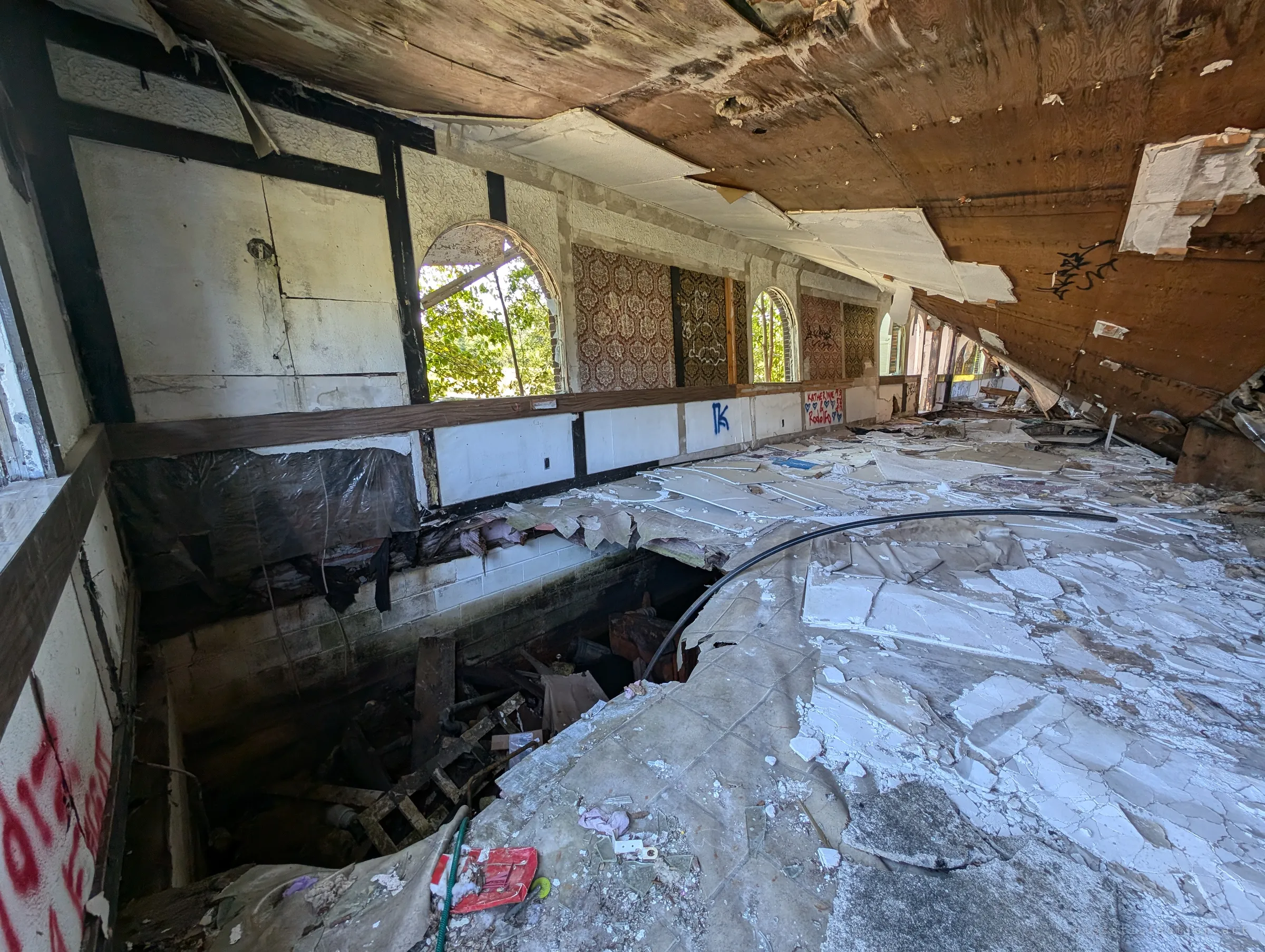A long hall of arched windows and damask wallpaper panels, the ceiling peeling down and the floor collapsed into the basement. The old decor hints at the place's better days.