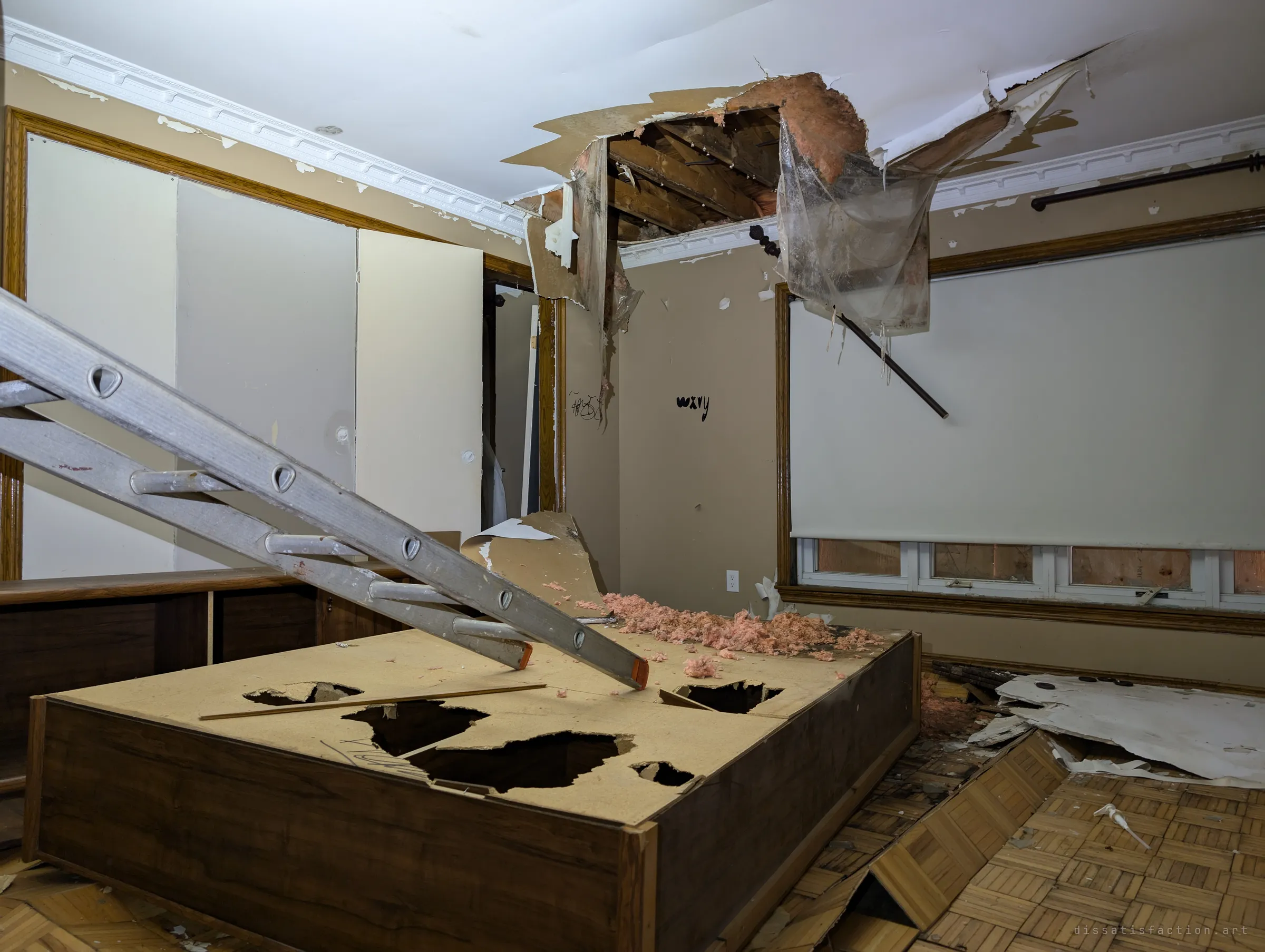 A ladder rests on a smashed platform bed under a hole torn through the ceiling, pink insulation spilling onto the floor. Boarded windows glow faintly behind a pulled-down blind.
