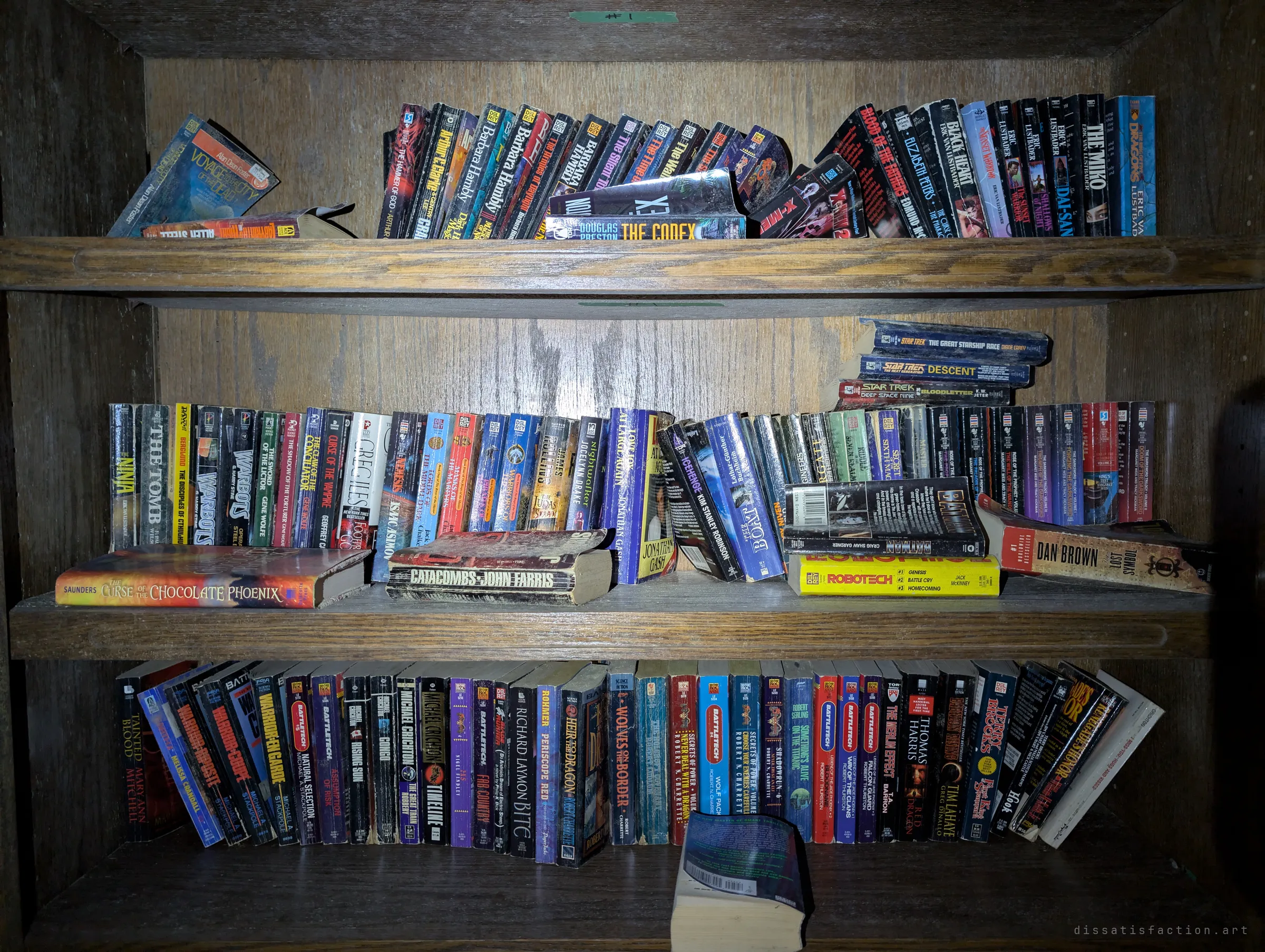 Three shelves of worn paperbacks, mostly sci-fi, fantasy and thrillers, left behind in a dark oak bookcase. A small personal detail of whoever lived here.