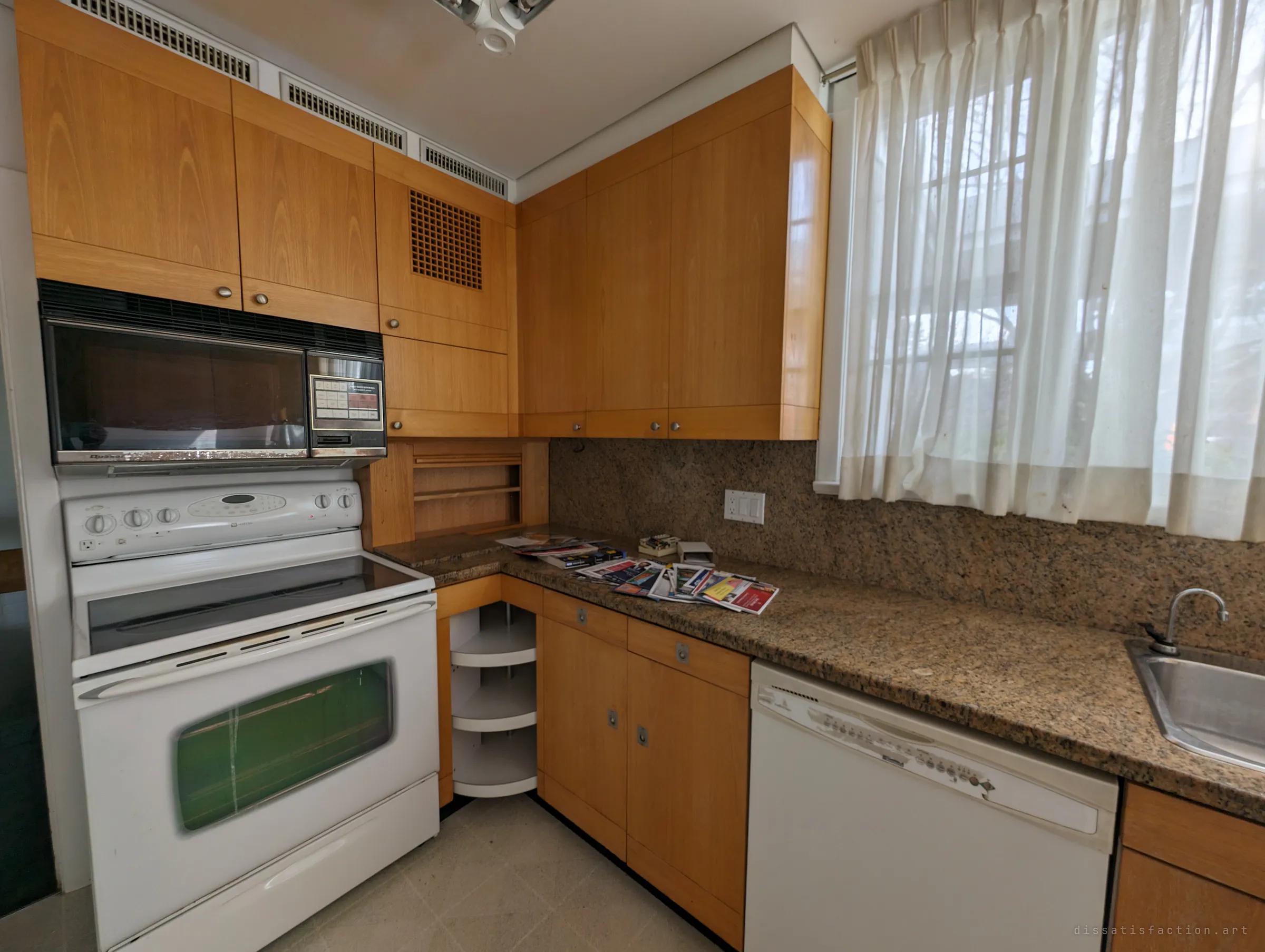 A wood-panelled kitchen with granite counters and an old white range, a pile of unread flyers left on the counter as if the owners just stepped out.