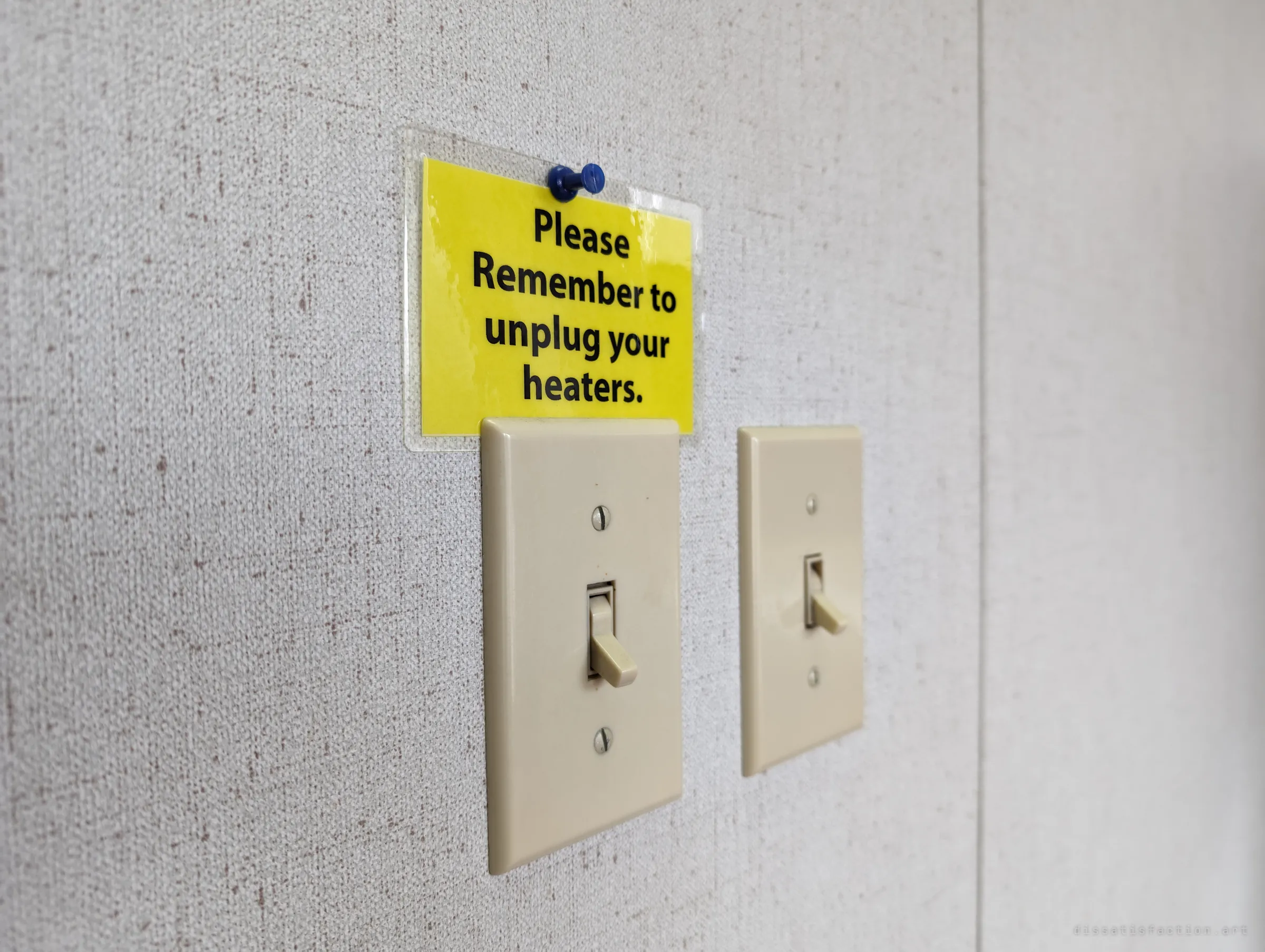 A laminated yellow note pinned above two light switches reminds staff to unplug their heaters. A small office habit outliving the office.