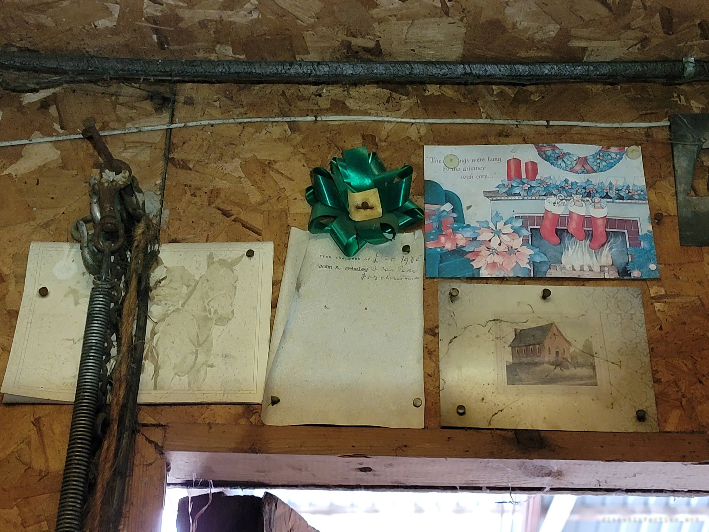 Faded pictures, a Christmas card, a memo sheet and a green gift bow still pinned above the workshop door, a small trace of the people who worked here.