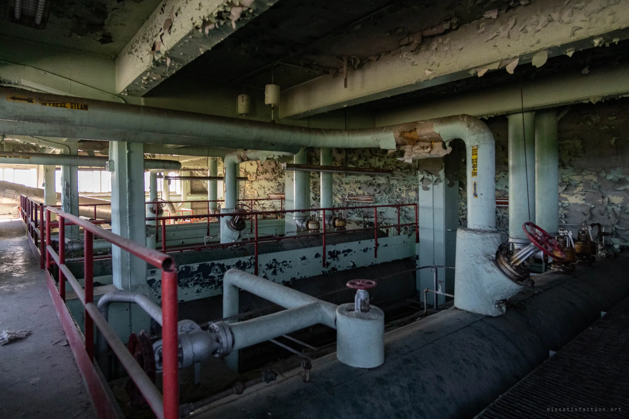 On the upper level, insulated high-pressure steam lines loop over the boiler drums, past red railings and walls of flaking paint.