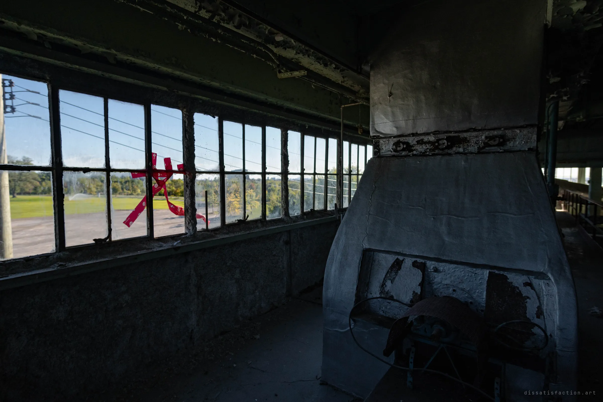 A dim upper room with a hulking ventilation hood, torn red tape stuck across the windows and a sunny open field outside.