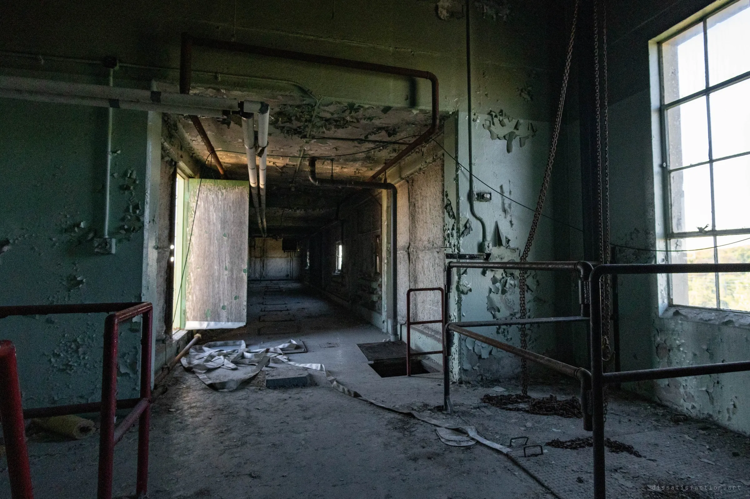 A top-floor landing with a fire hose tangled on the floor, an open trapdoor and a hanging chain hoist, and a dim corridor running back.