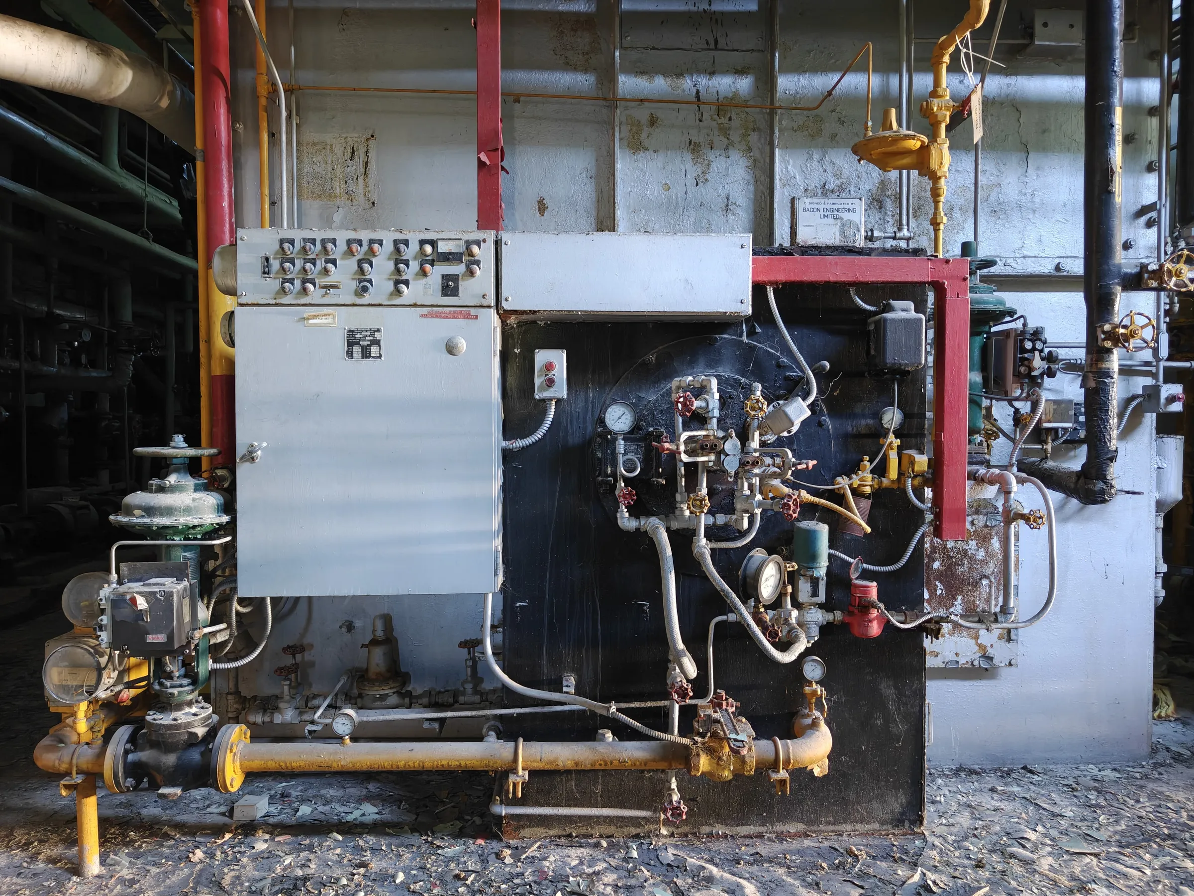 Front of a packaged boiler: a grey push-button control cabinet, a black burner plate crowded with gauges and valves, and a yellow gas train along the floor. A straight-on record of how the burners were controlled.