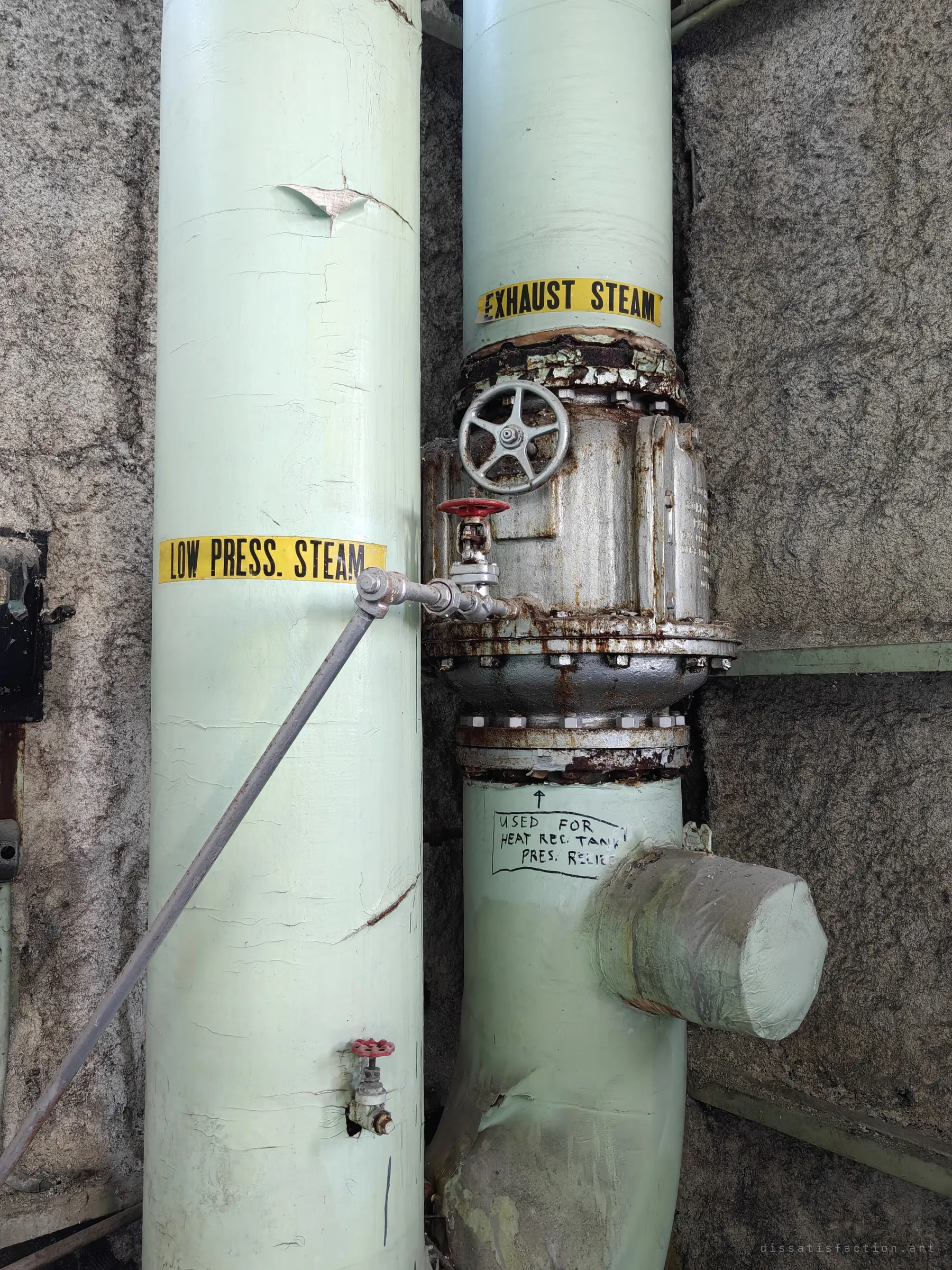 Two pale green insulated pipes labelled for low pressure and exhaust steam, one fitted with a big flanged valve and a handwritten note about pressure relief. The labels spell out how the plant moved its steam.