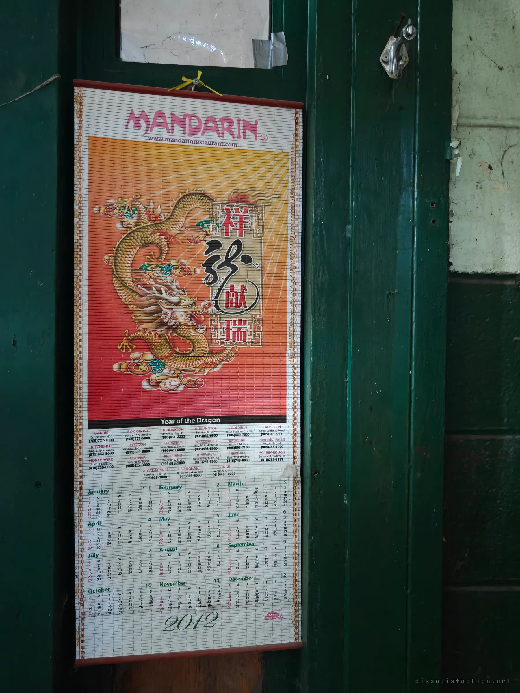A bamboo wall calendar from 2012 with a golden dragon, still hanging on a green-painted door frame. It marks roughly when the staff last kept track of the days here.