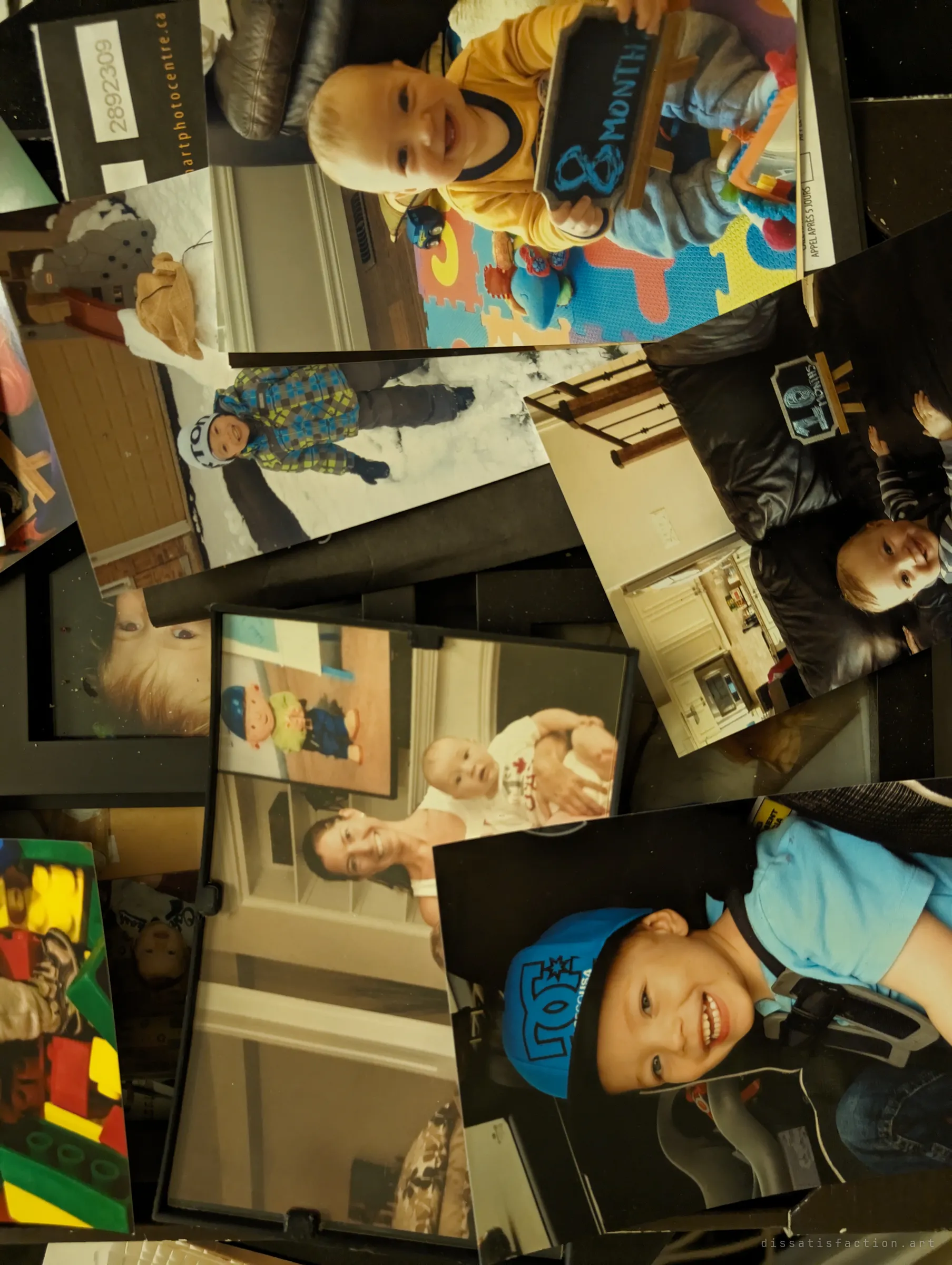 A scattered pile of printed family snapshots, mostly a baby and toddler growing up, some with month-count chalkboards. Years of a family's life left behind.