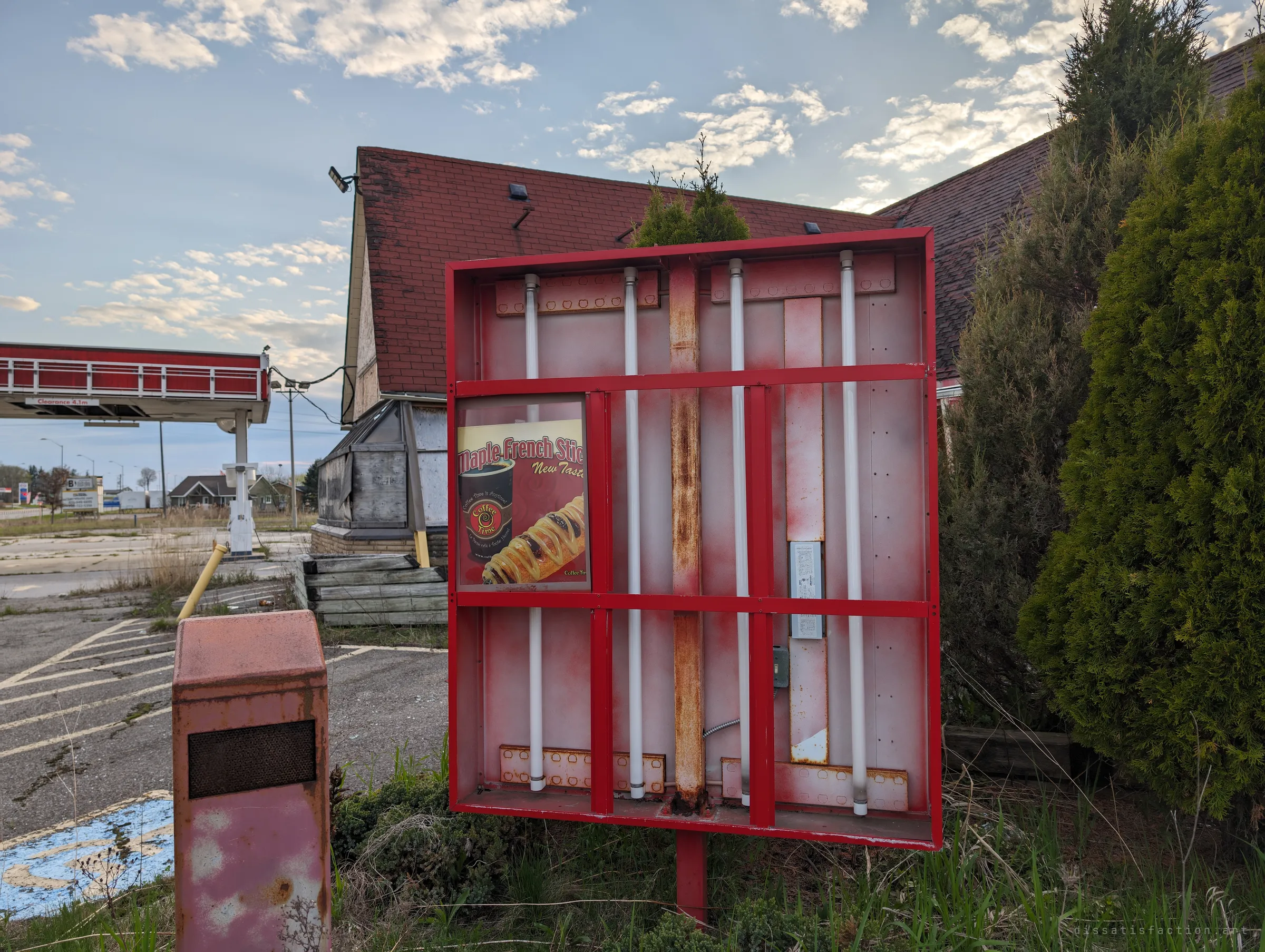 An emptied roadside sign box, fluorescent tubes still standing inside, with one leftover coffee-and-pastry ad in the corner and the abandoned restaurant behind.