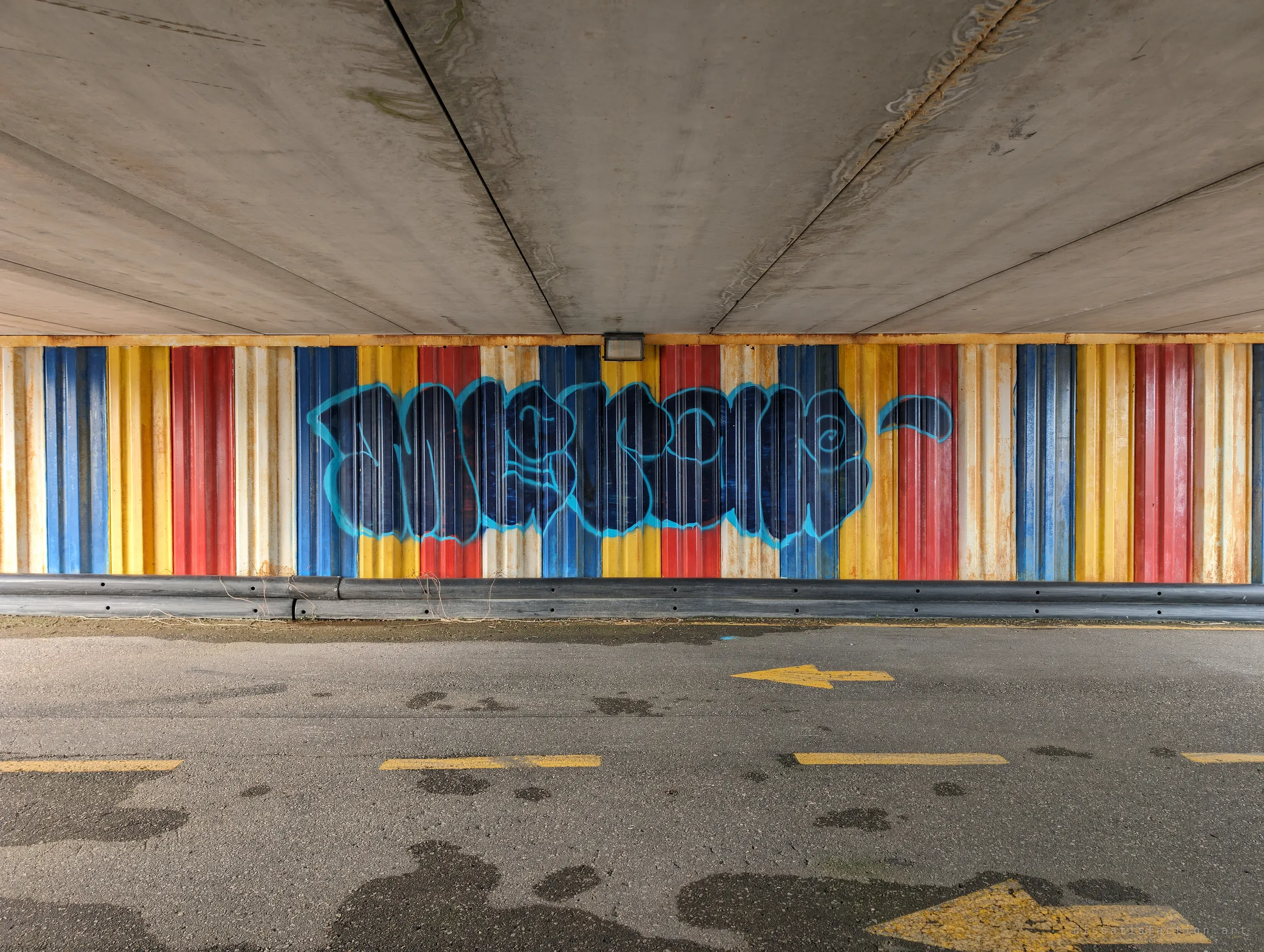 Under the bridge, a large blue graffiti piece stretches across the red, yellow and blue corrugated wall above the painted track arrows.