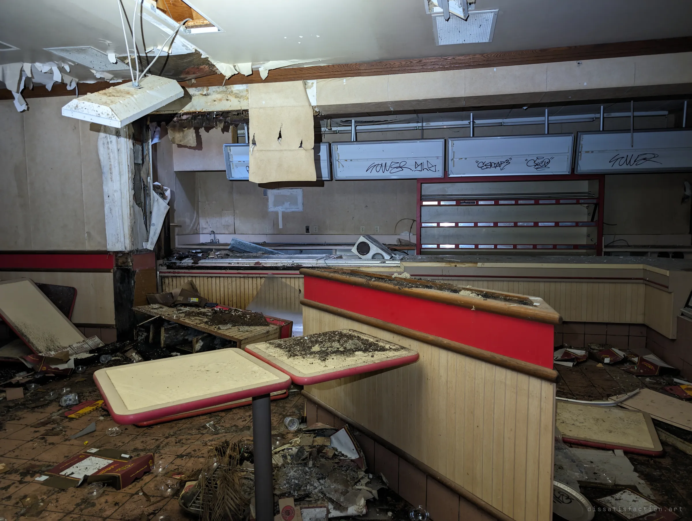 The restaurant's service counter lies wrecked: ceiling panels hang loose, tagged menu boards sit dark and old pizza boxes litter the tiled floor.