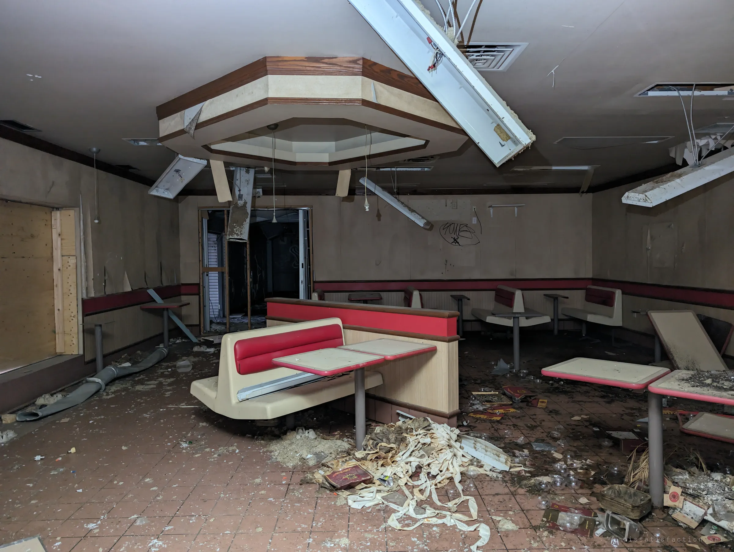 The dining room of the abandoned restaurant, booths still bolted in place beneath collapsed light fittings and a drift of debris across the tiles.